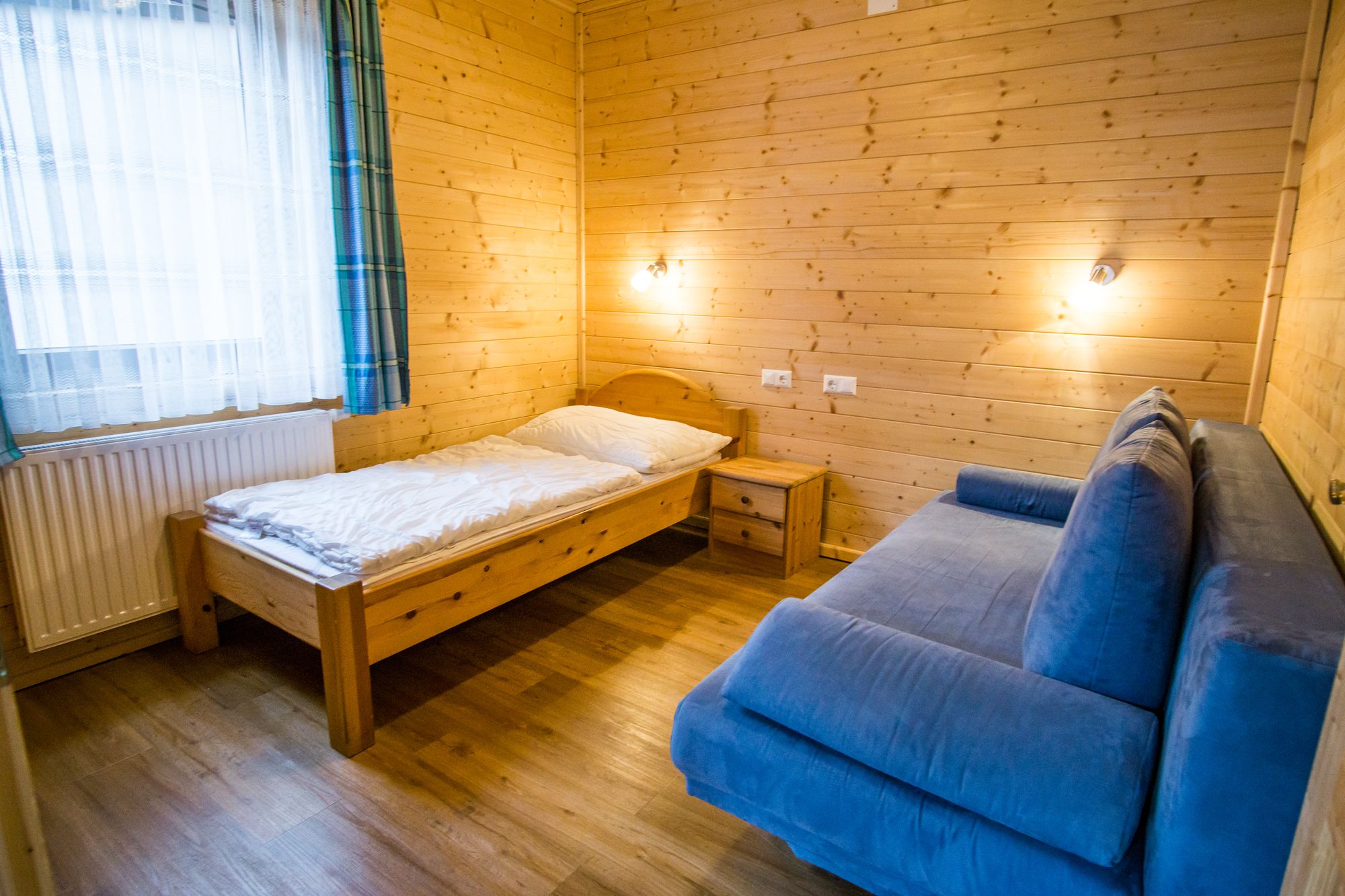 Gyerekszoba fából készült falakkal, egyszemélyes ággyal, kék kanapéval és éjjeliszekrénnyel.