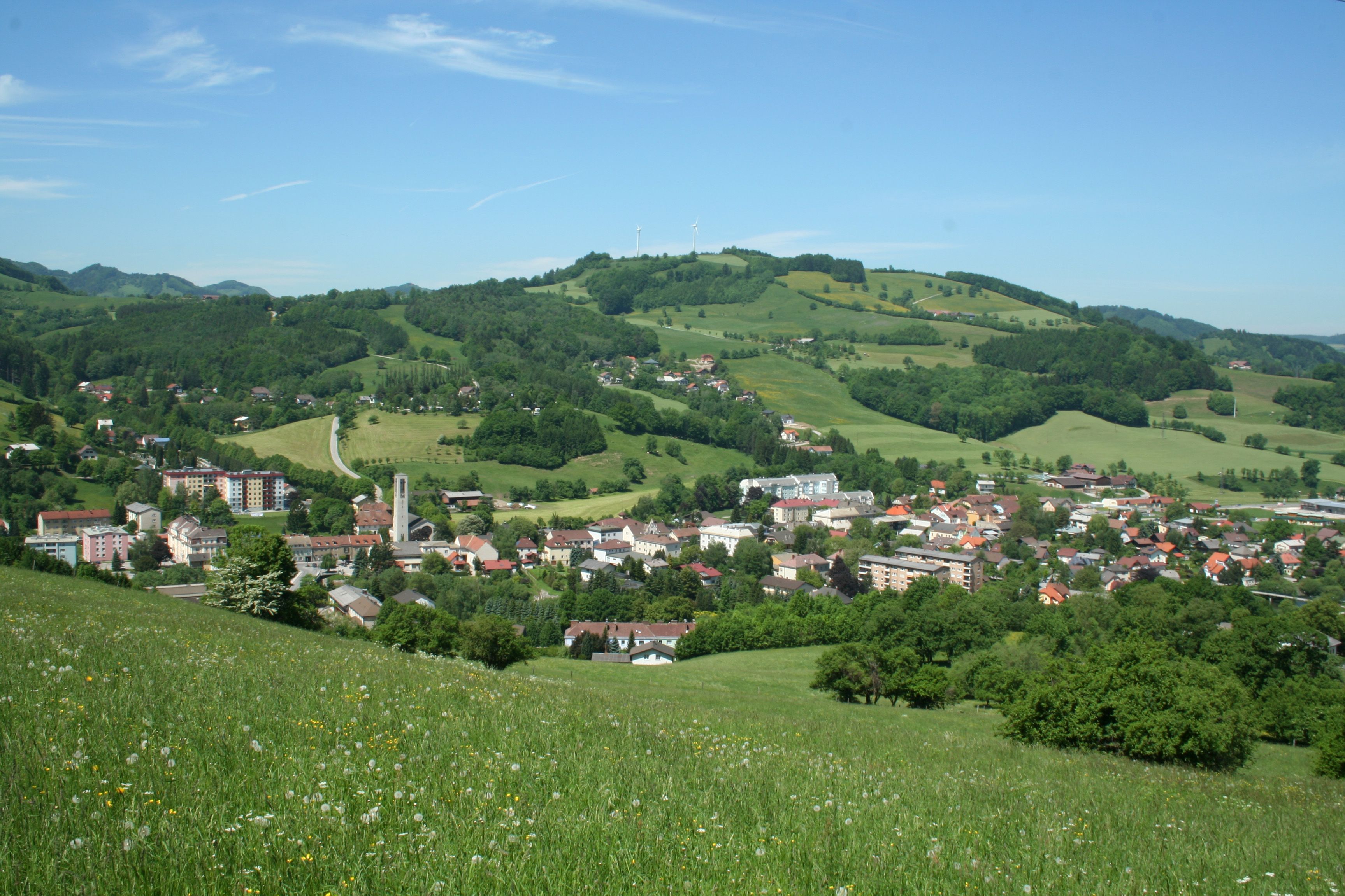 Traisen városának panorámaképe zöld dombokkal és szélturbinákkal a háttérben.