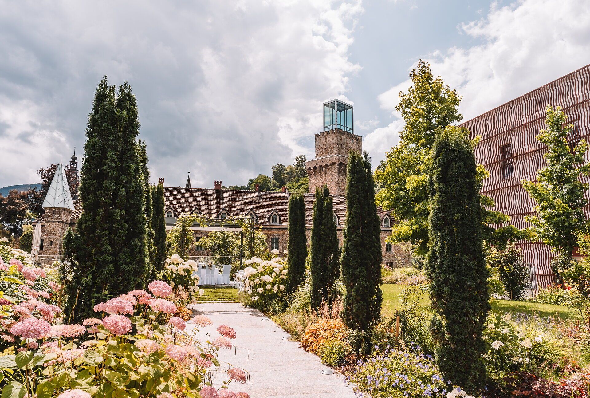 Blühender Schlossgarten von Schloss Rothschild in Waidhofen an der Ybbs mit Blumenbeeten, schlanken Zypressen und dem gläsernen Turm des historischen Gebäudes