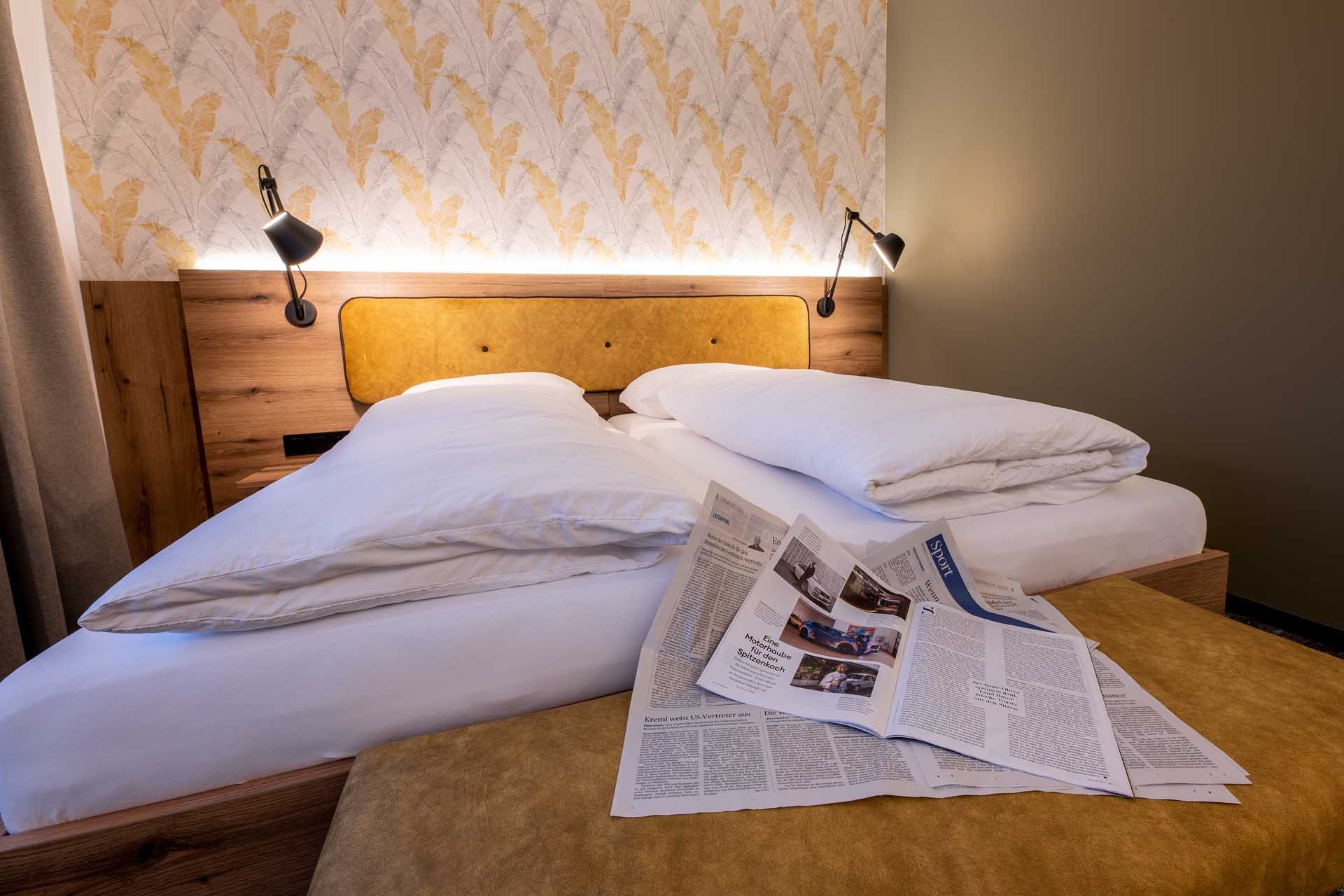 Hangulatos vendégszoba franciaággyal, újságokkal a paplanon és stílusos tapétával a háttérben.