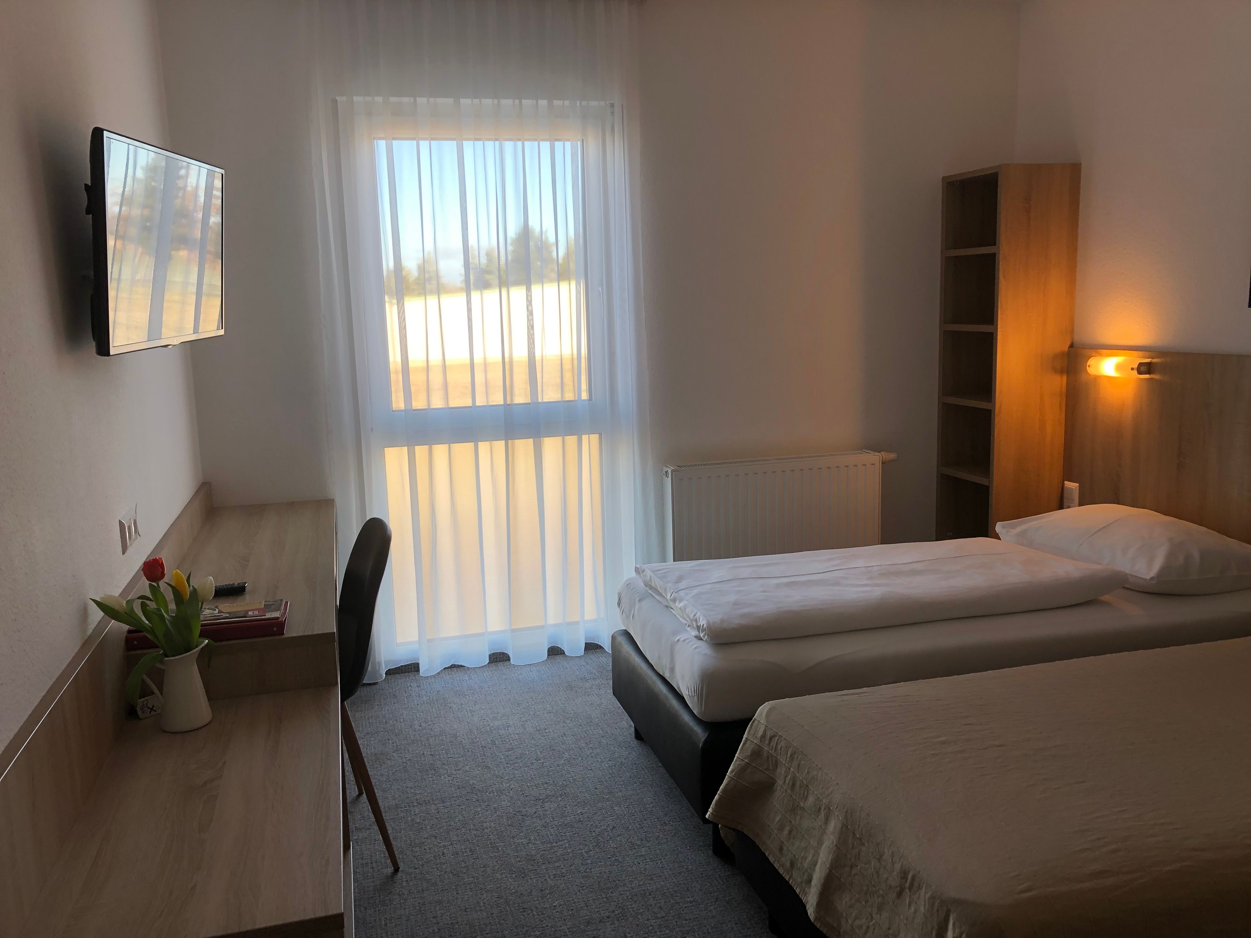 Egyszerűen berendezett motelszoba két egyszemélyes ággyal, íróasztallal, televízióval és függönyös ablakkal.