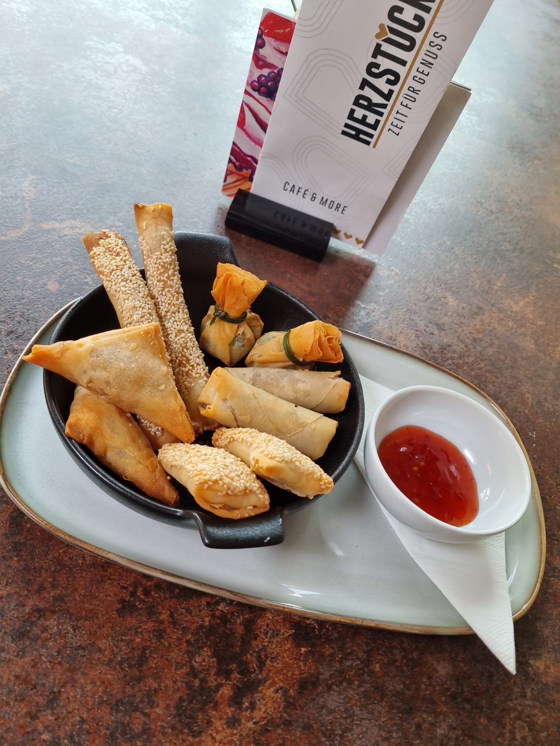 Különböző sült rágcsálnivalók egy tányéron, mártogatós és kávézó étlapja a háttérben.