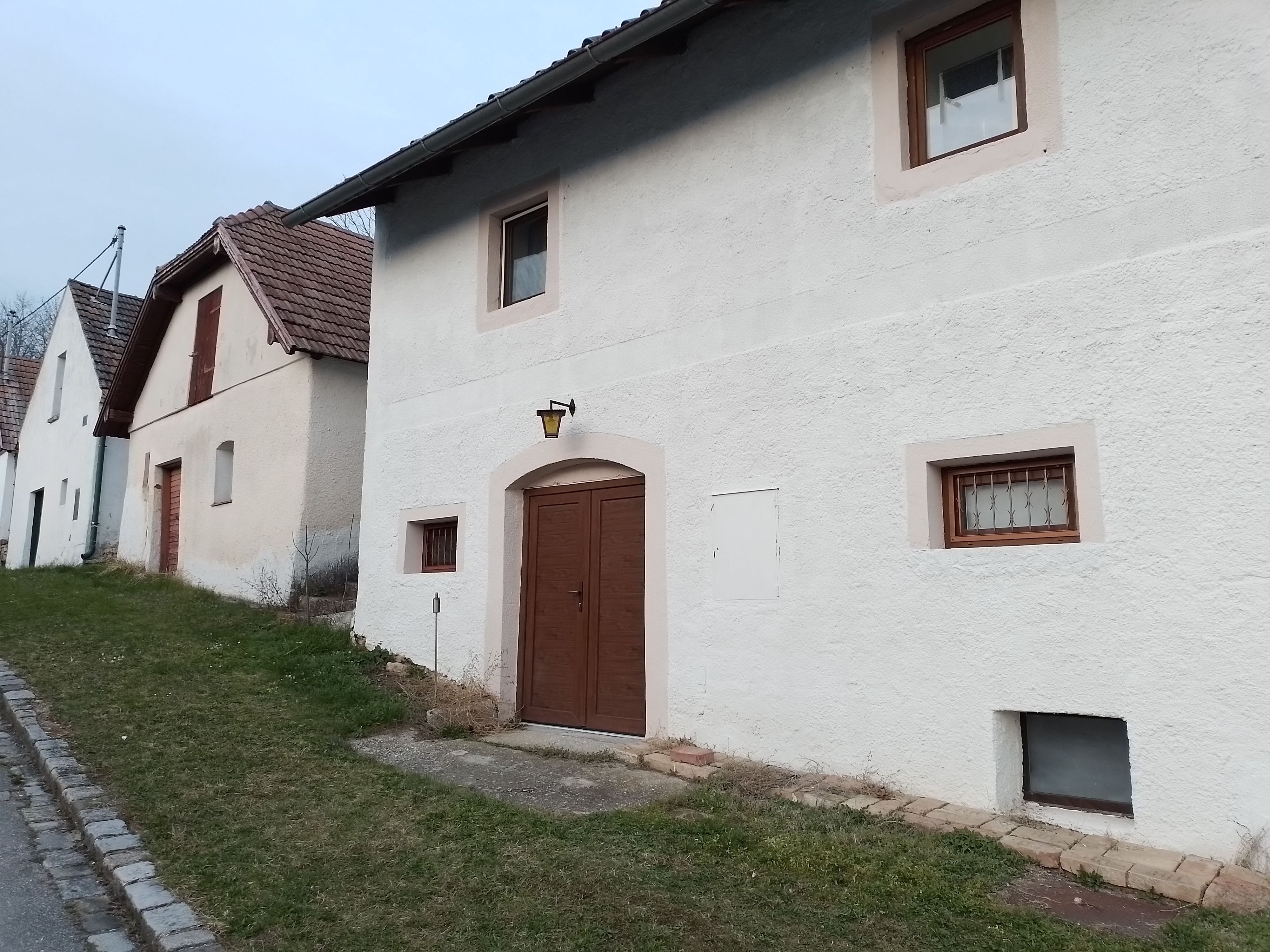 Fehér házak sora, barna ajtókkal és ablakokkal, egy füves út mentén.