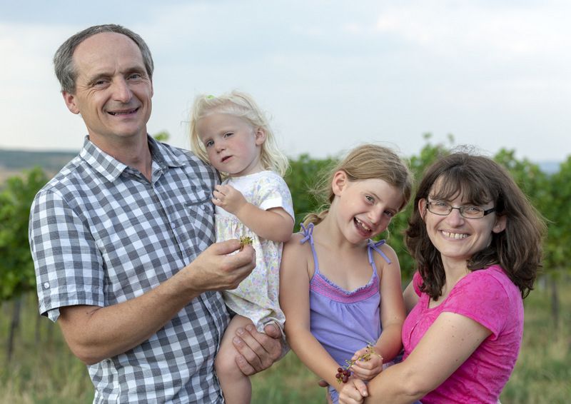 Egy család áll mosolyogva egy szőlőben.