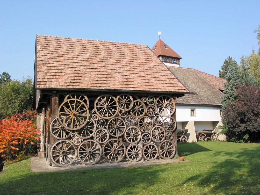 Egy épület, amelynek homlokzata régi szekérkerekekből készült, fákkal és pázsittal körülvéve.