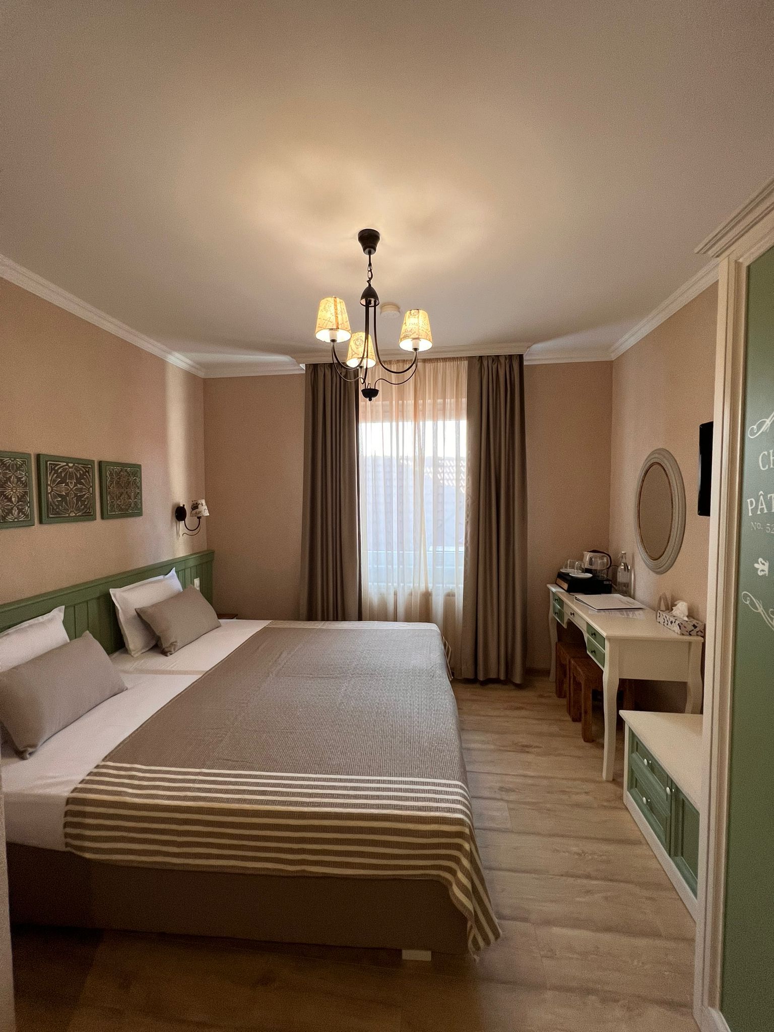 Hangulatos szállodai szoba franciaággyal, íróasztallal és függönyös ablakkal.