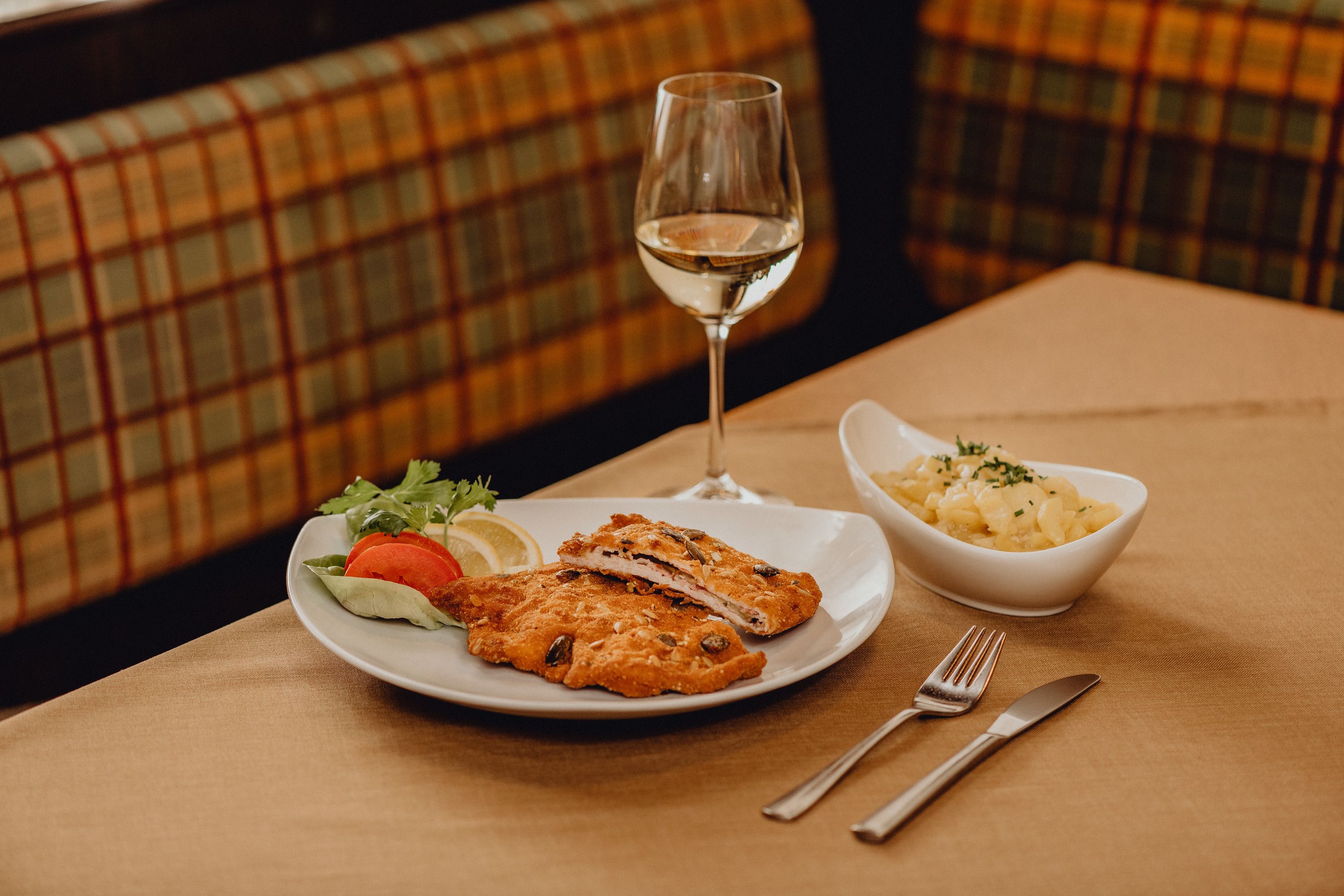 Egy tányér cordon bleu, saláta körettel és egy pohár fehérborral az asztalon.