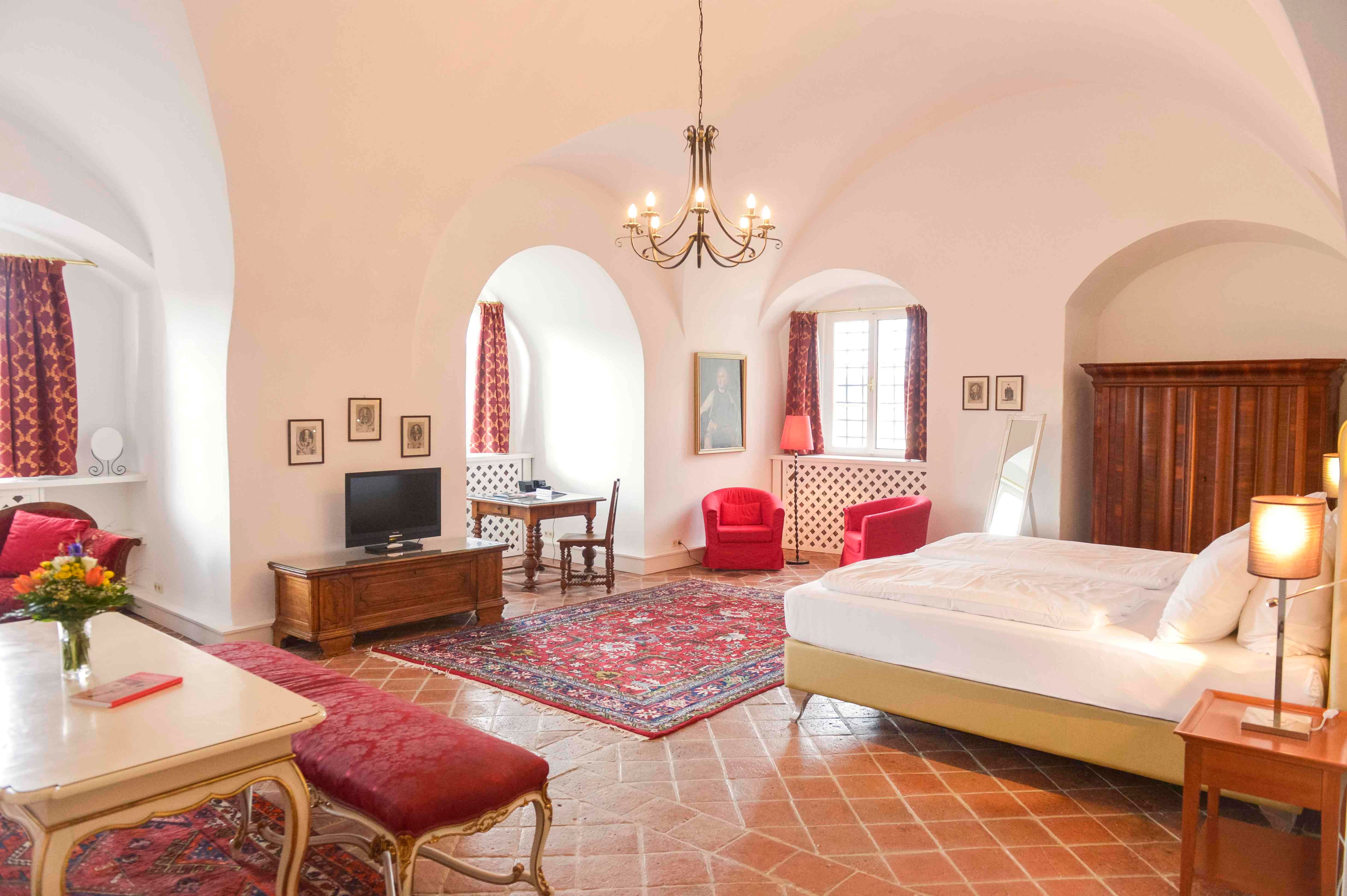 Luxus lakosztály antik bútorokkal, vörös szőnyegekkel és függönyökkel, nagy ággyal és csillárral.