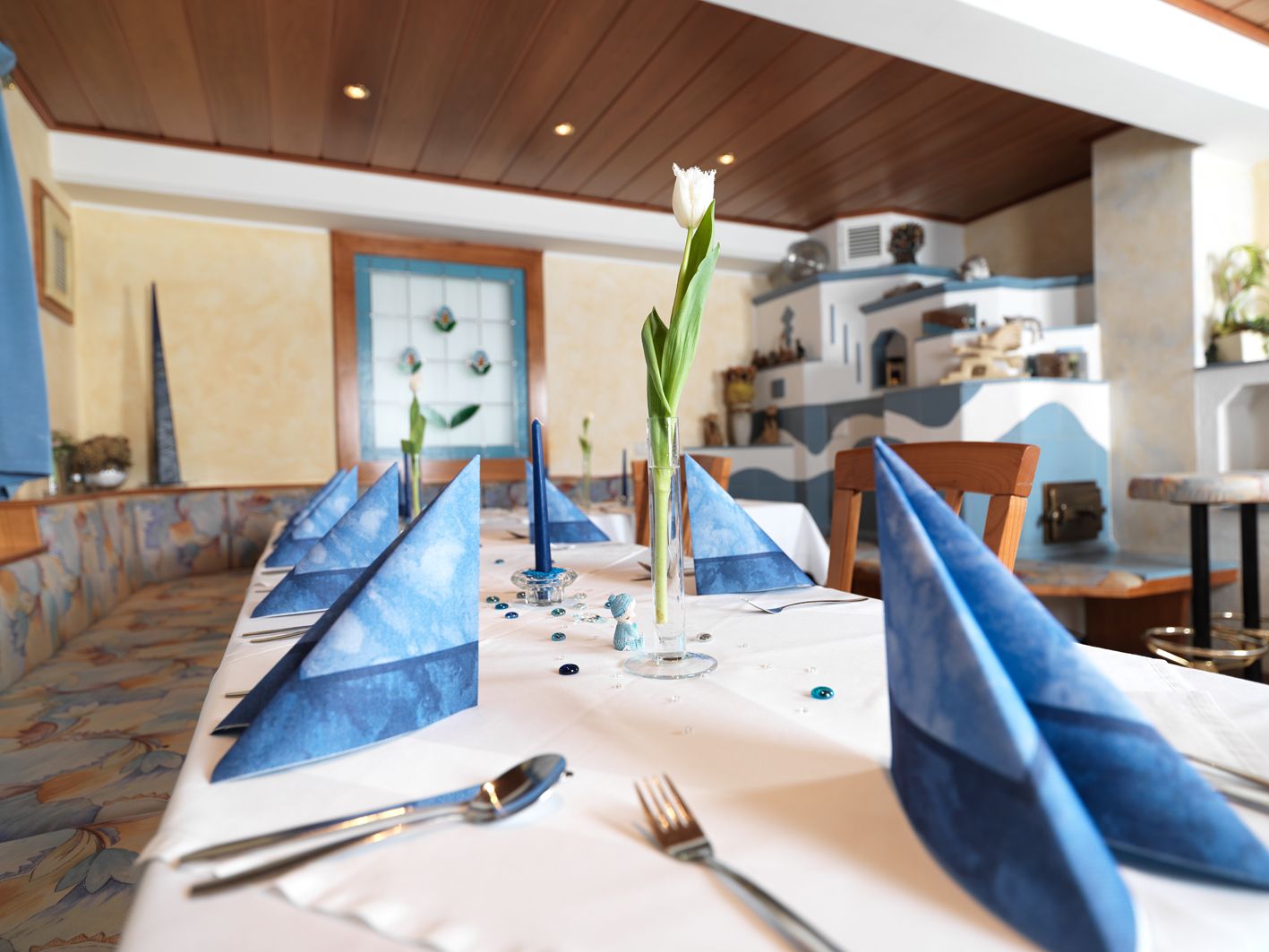 Elegánsan megterített asztal, kék szalvétákkal és egy pohárban fehér tulipánnal egy hangulatos szobában.