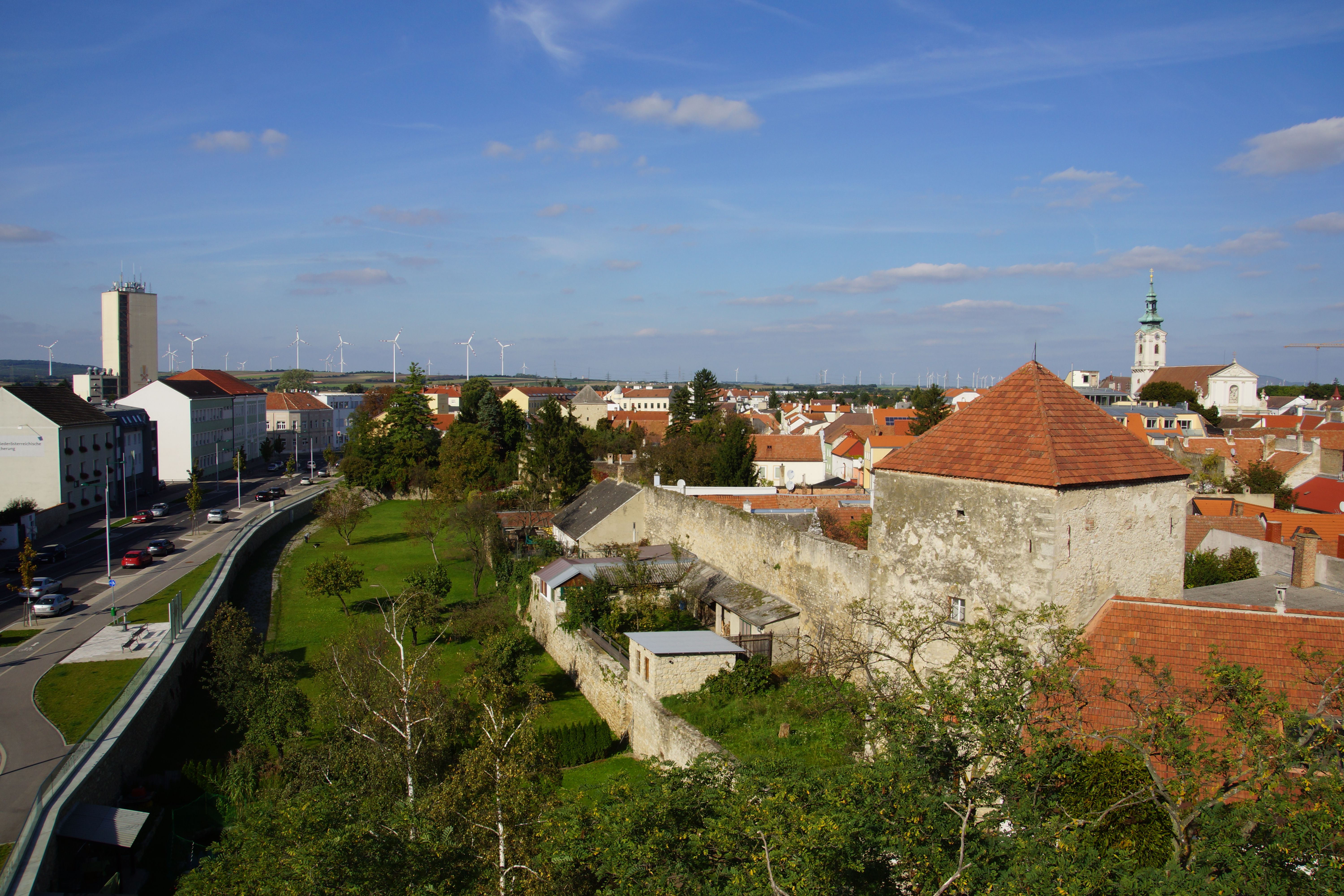 Bruck an der Leitha városnézete, háttérben a városfal, a templom és a szélturbinák.