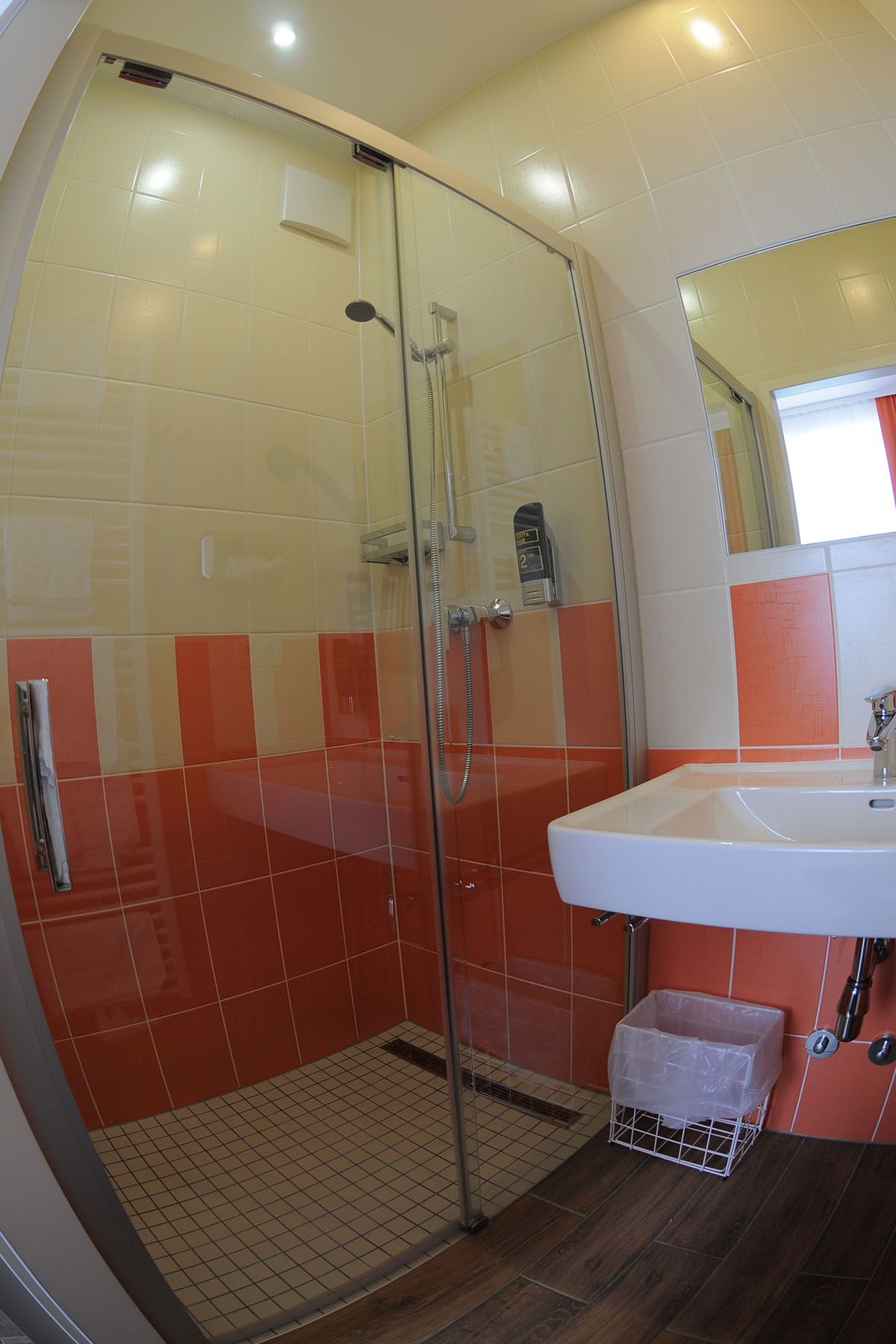 Fürdőszoba zuhanyzóval, mosdókagylóval, narancs és fehér csempével.