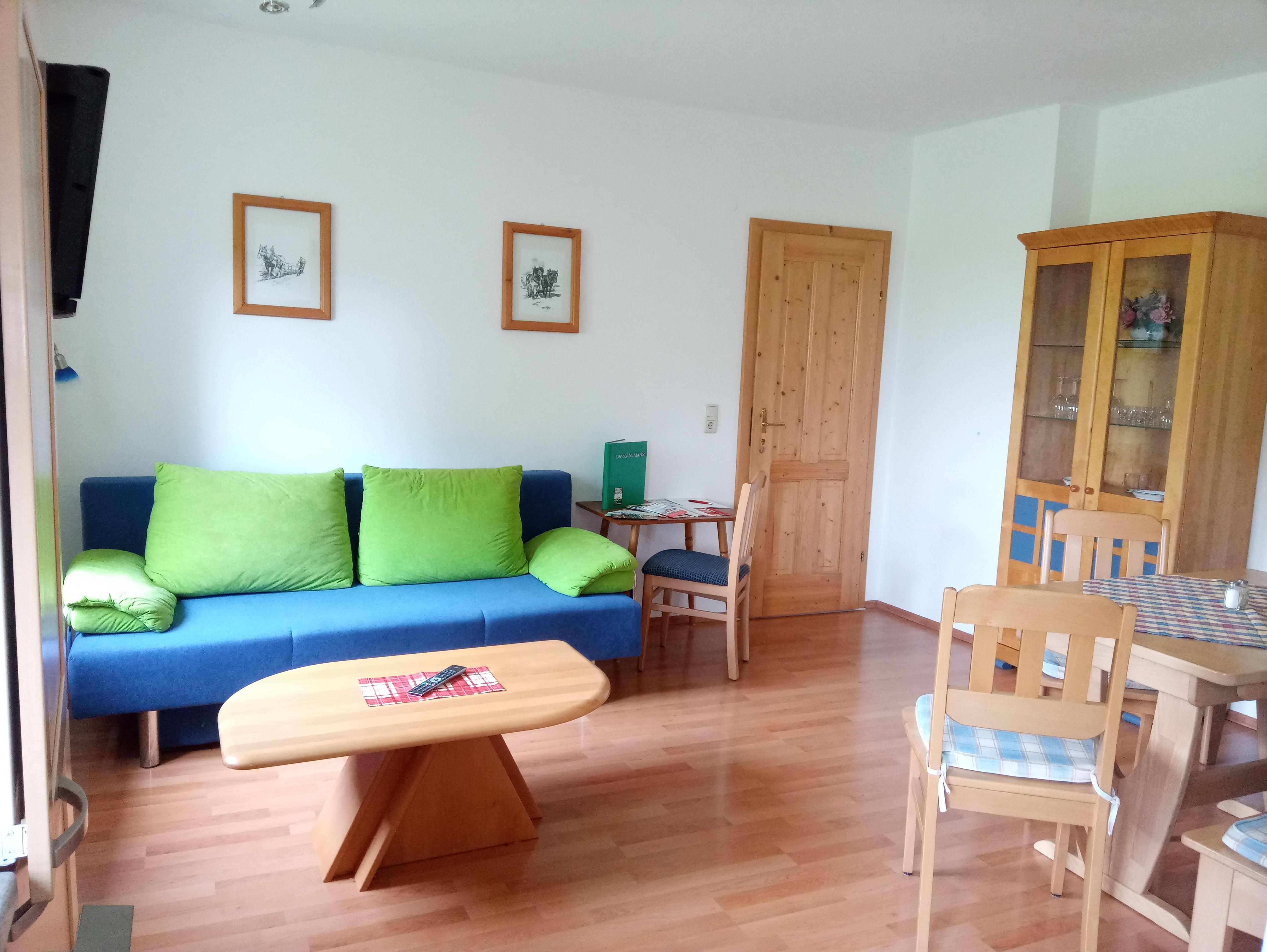 Nappali kék kanapéval, fa asztallal és székekkel, szekrénnyel és képekkel a falon.