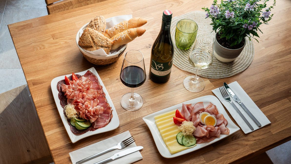 Egy asztal regionális finomságokkal: Sajtok, kenyér, vörös- és fehérbor.