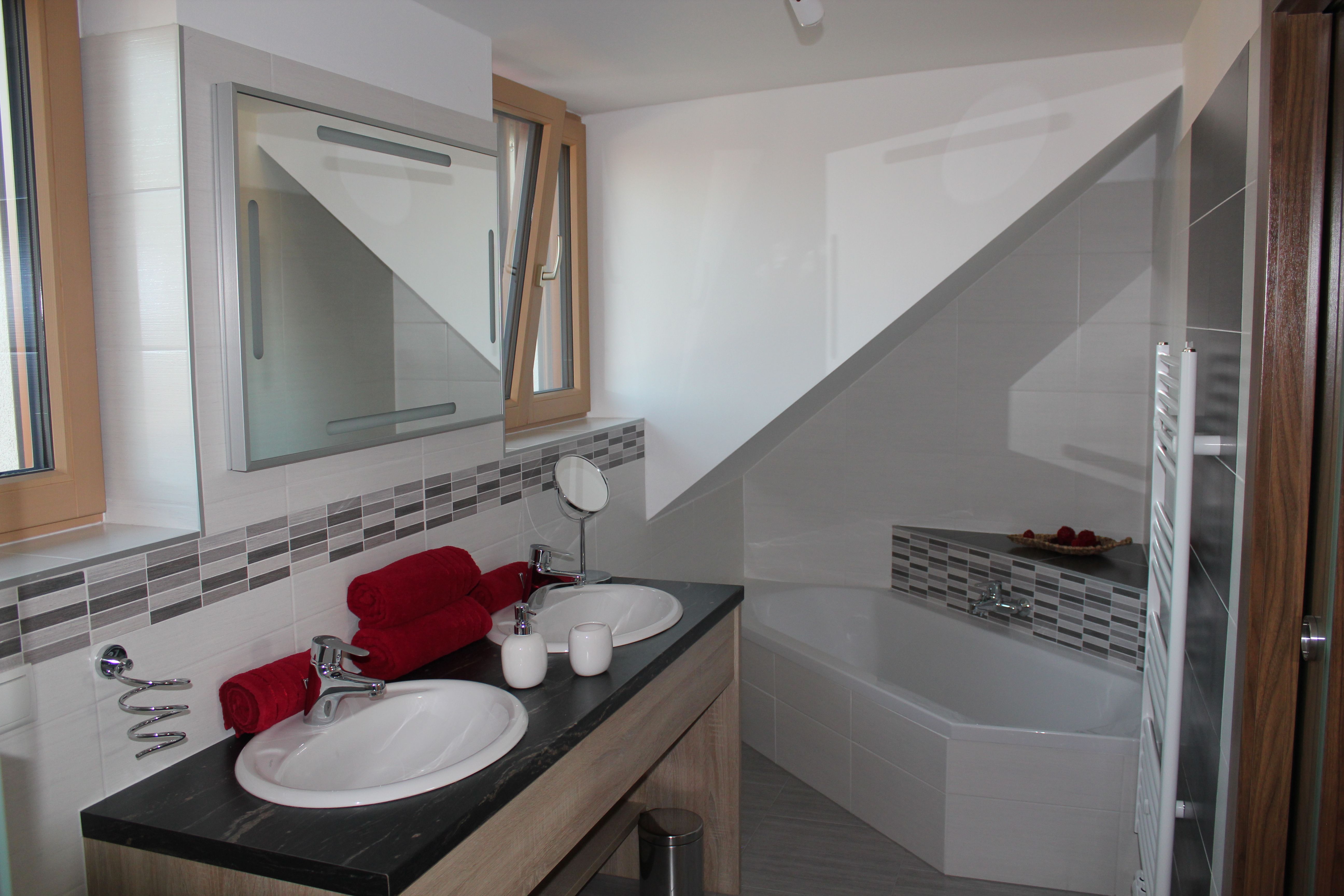 Modern fürdőszoba dupla mosdóval, káddal és piros törölközőkkel.