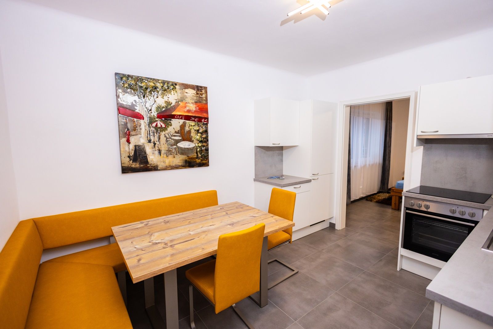 Modern konyha sárga sarokpaddal, fa asztallal és művészeti alkotásokkal a falon.