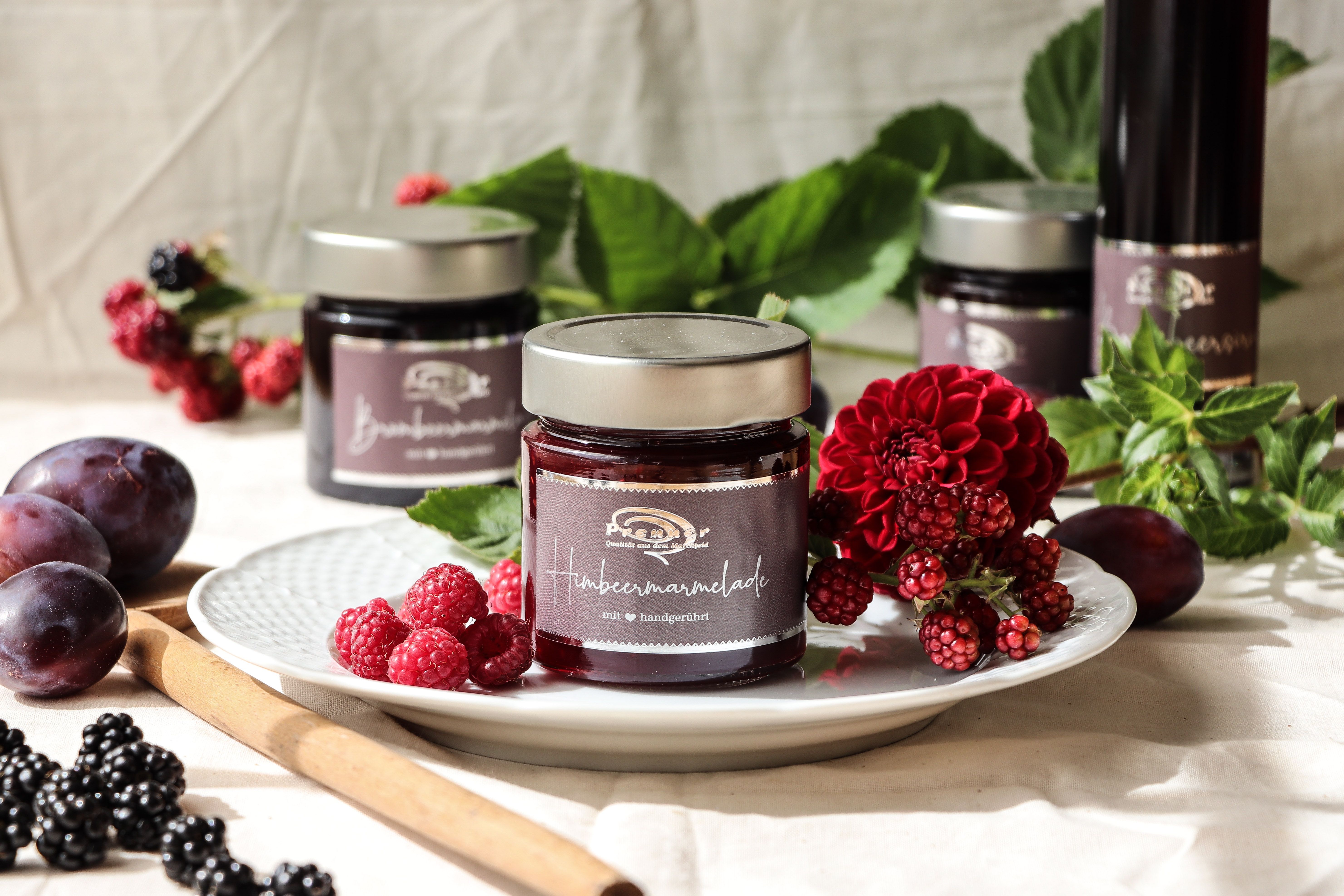 Egy üveg málnalekvár egy tányéron, friss bogyós gyümölcsökkel és virágokkal díszítve.