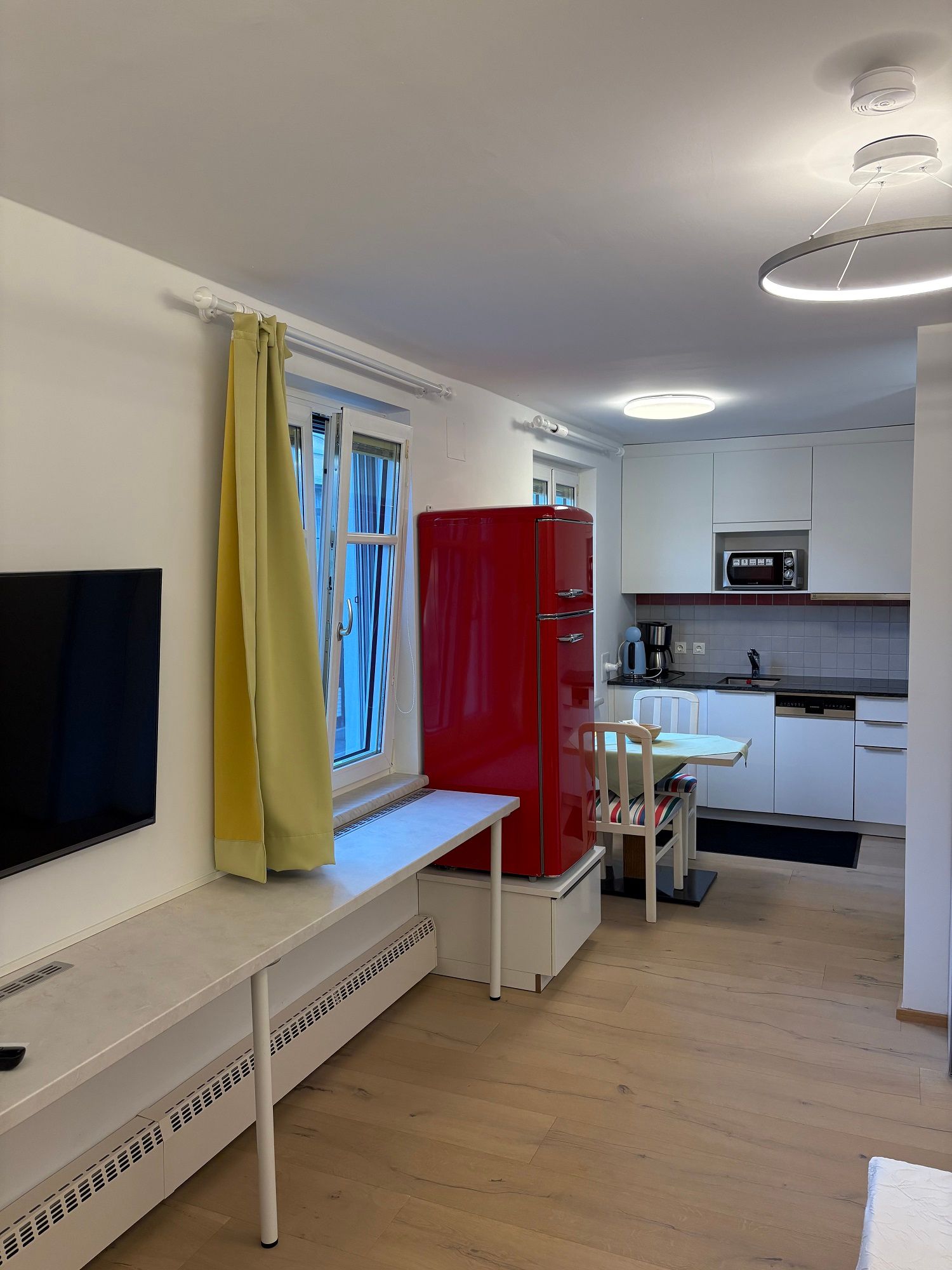 Modern nappali nyitott konyhával, piros hűtőszekrénnyel, sárga függönyökkel és fapadlóval.
