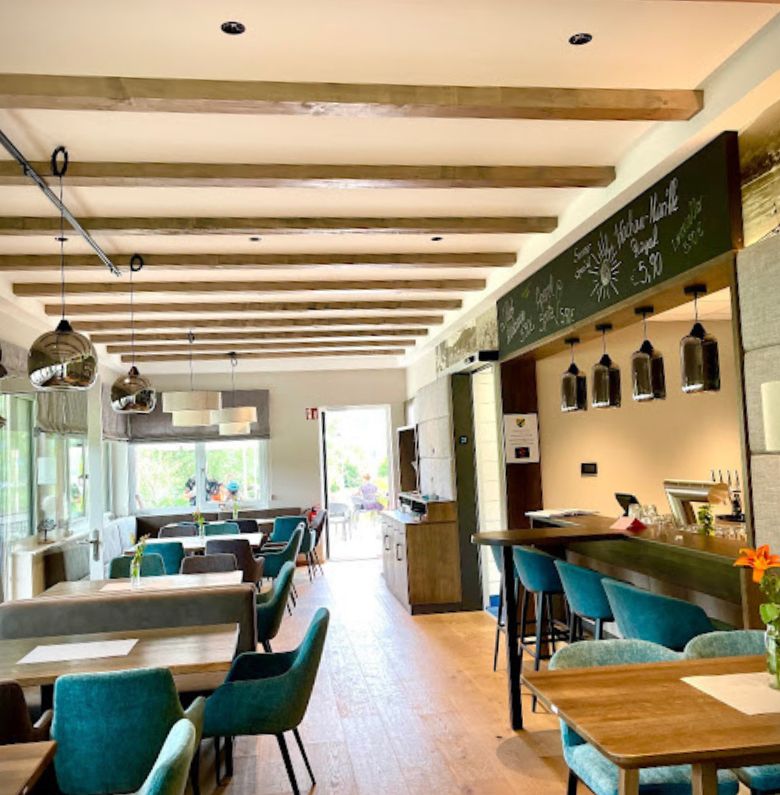 Belső éttermi rész asztalokkal és zöld fotelekkel