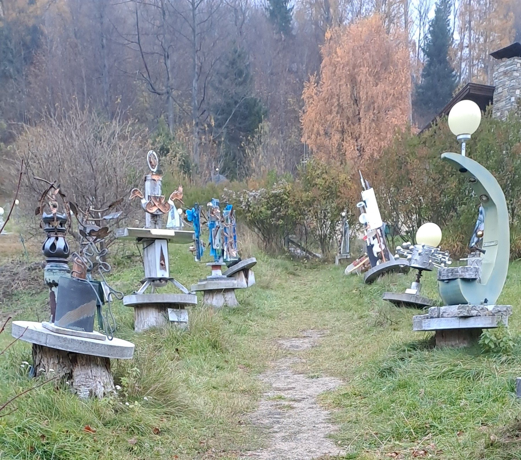 A Semmering szoborparkban egy ösvény, amelyet fából készült talapzaton álló absztrakt fémszobrok szegélyeznek, és őszi növényzet vesz körül.