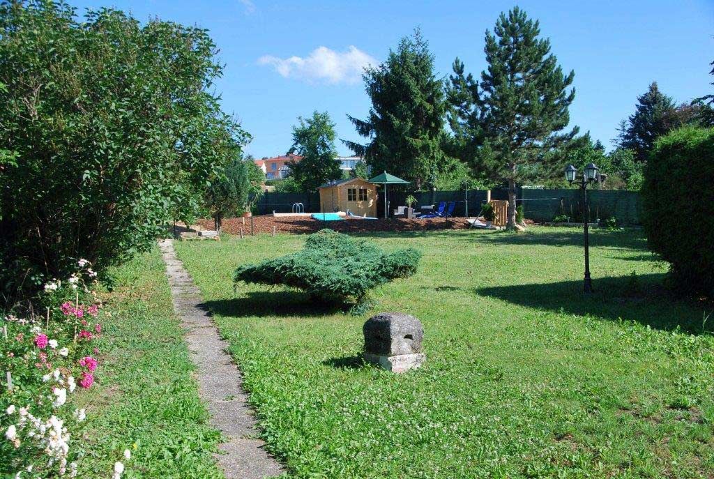 Kert pázsittal, fákkal és egy kis ösvény vezet egy faházhoz.