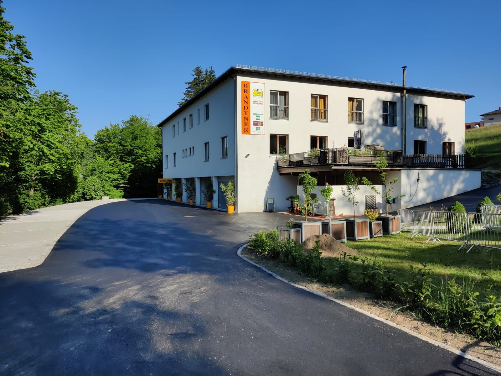 "Brandtner" feliratú épület, fákkal és parkolóval körülvéve.