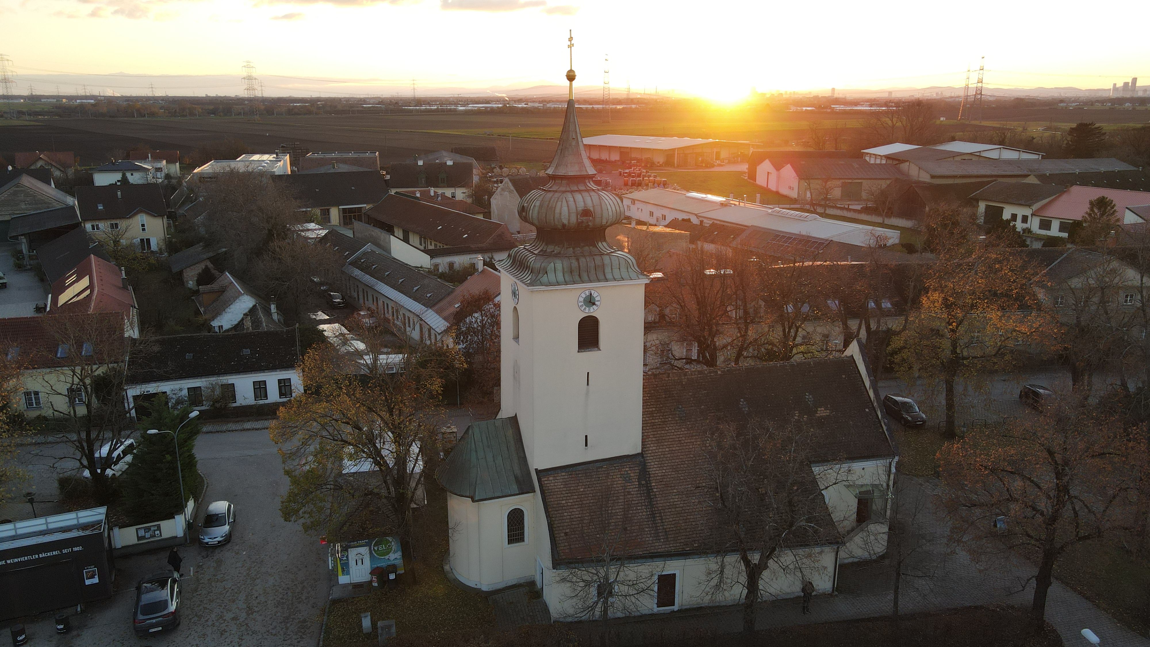 A Raasdorfi templom tornyával és hagymakupolájával naplemente idején, házak és mezők között.