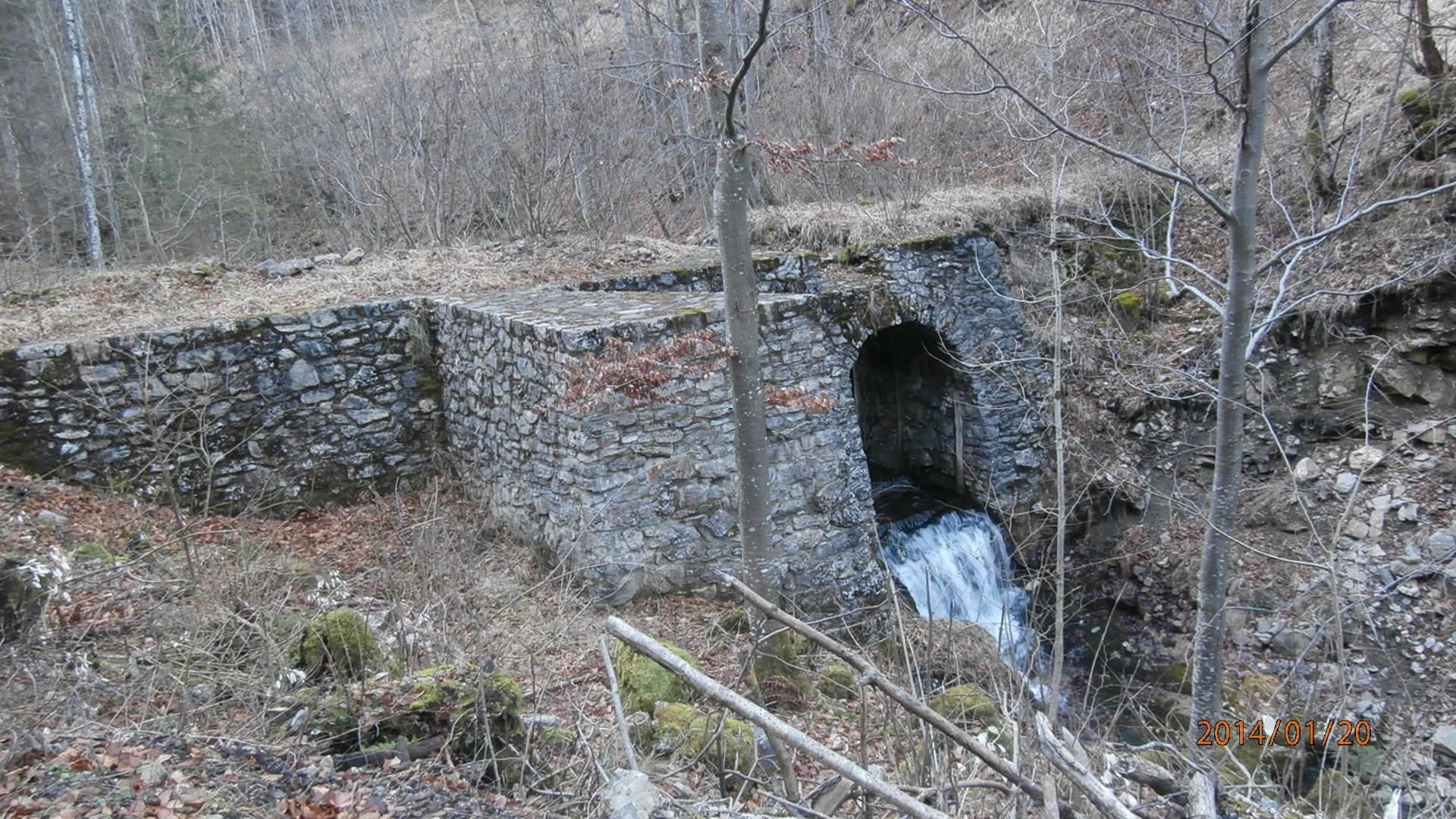 Kőfal vízeséssel, erdős környezetben.
