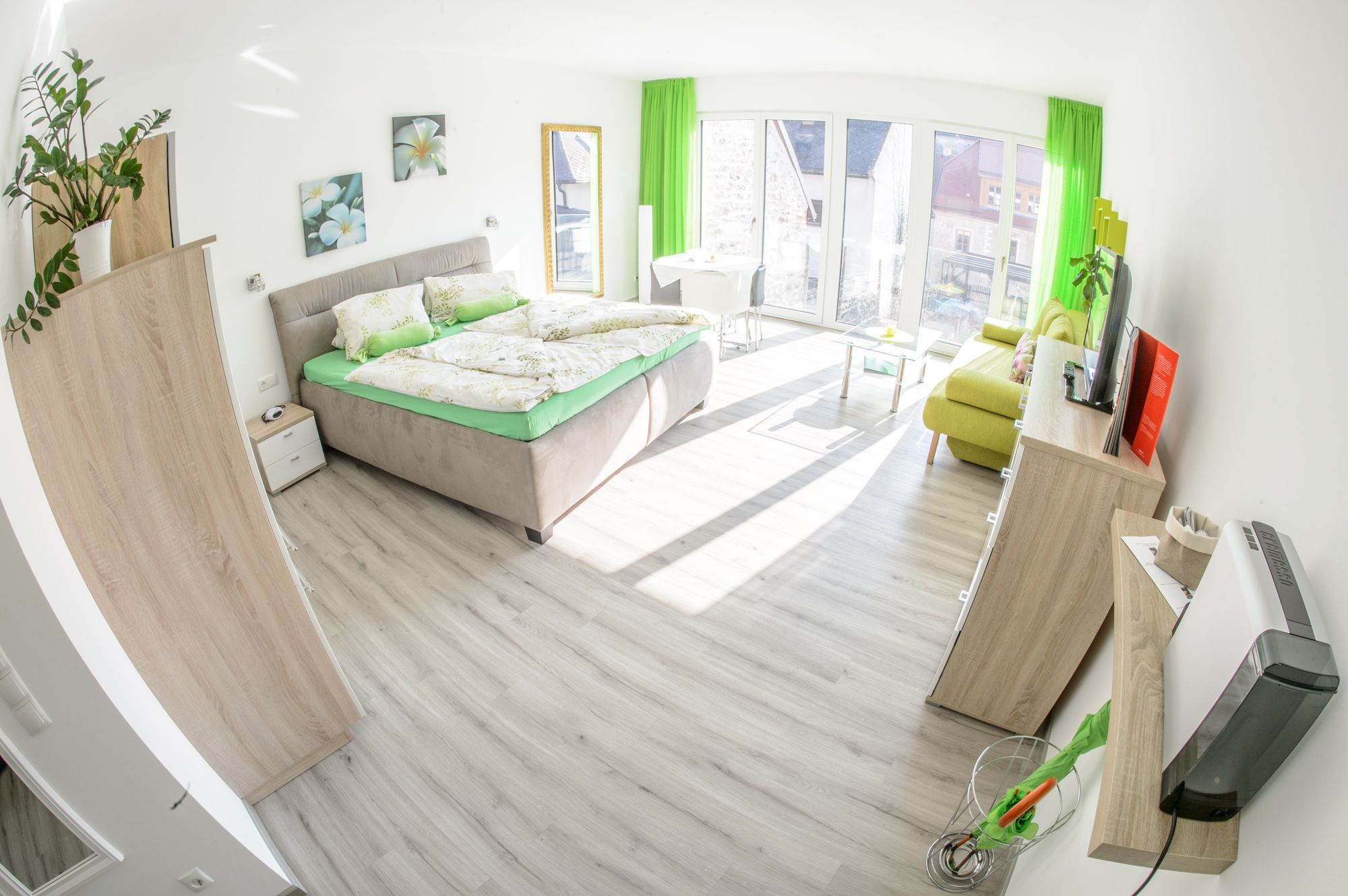 Világos vendégszoba franciaággyal, kanapéval, TV-vel és nagy ablakokkal.