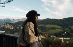 In der sanften Abenddämmerung genießt eine Frau die atemberaubende Aussicht auf die umliegenden Berge und Täler. Die frische Bergluft und die malerische Landschaft laden dazu ein, die Seele baumeln zu lassen und die Schönheit der Natur zu erleben.