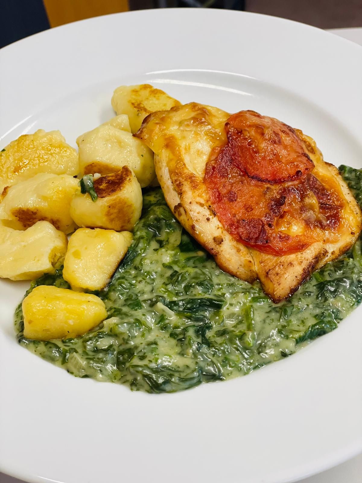 Tányér gnocchival, krémes spenóttal és gratinált csirkével, paradicsomszelettel.