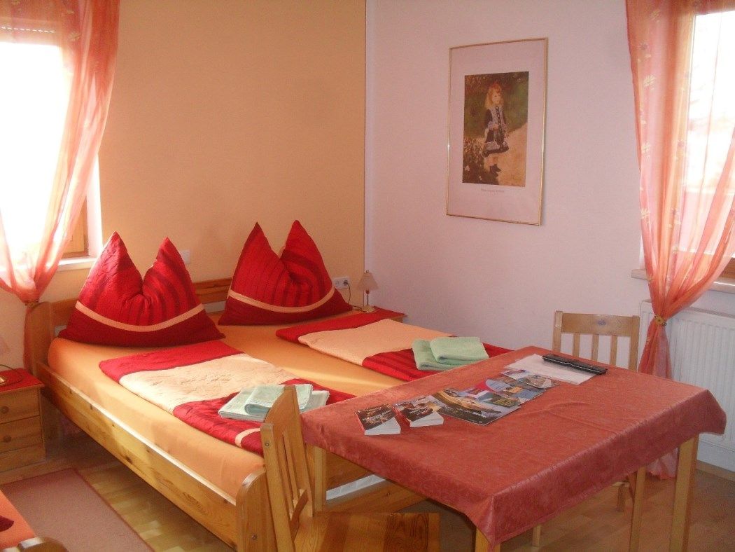 Hangulatos hálószoba franciaággyal, piros párnákkal és prospektusokkal teli asztallal.