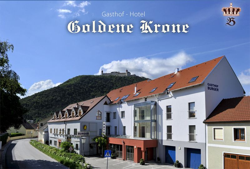 Gasthof-Hotel Goldene Krone egy erdős domb előtt, a háttérben egy kastéllyal.