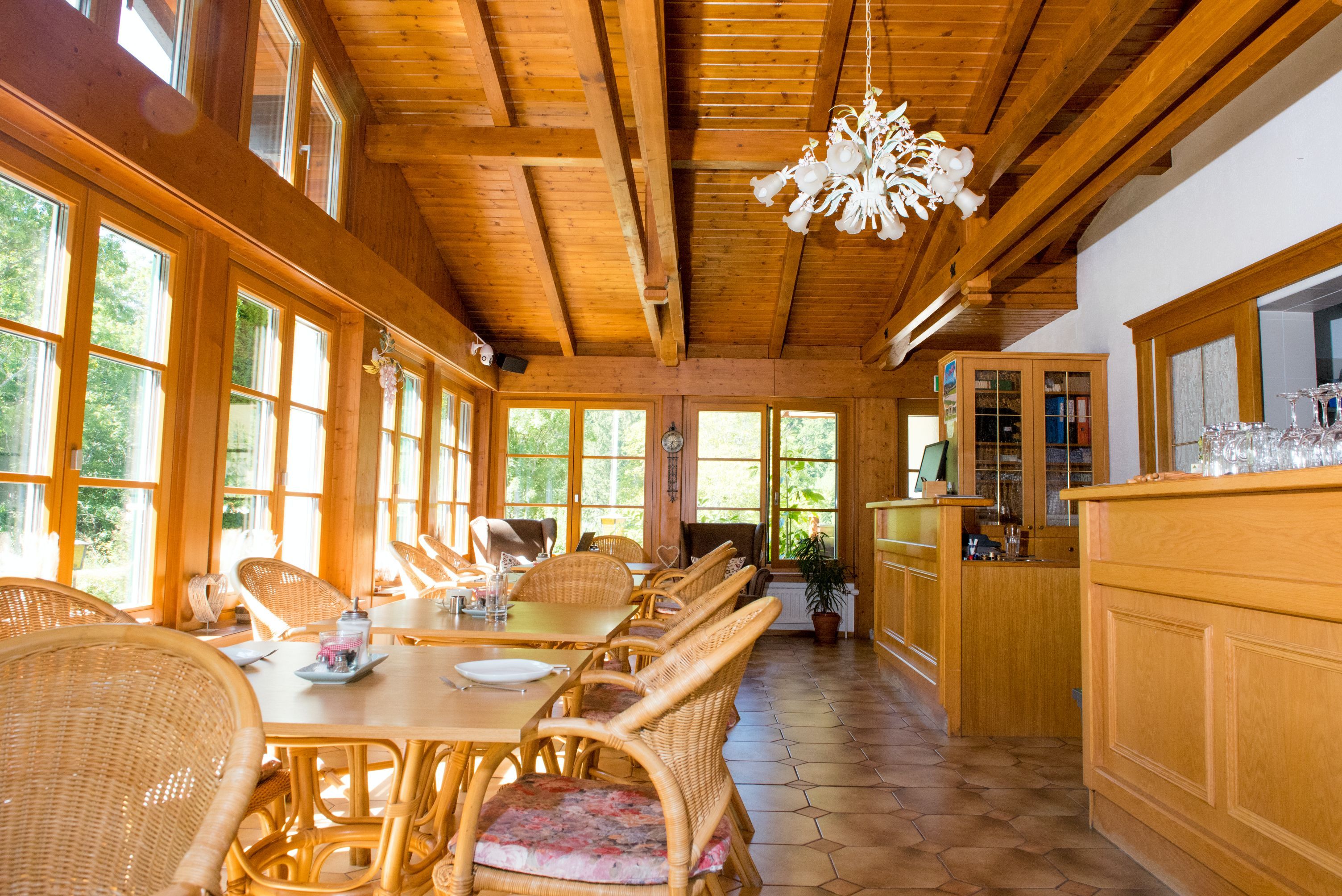 Világos reggelizőterem fabútorokkal, nagy ablakokkal és csillárral.