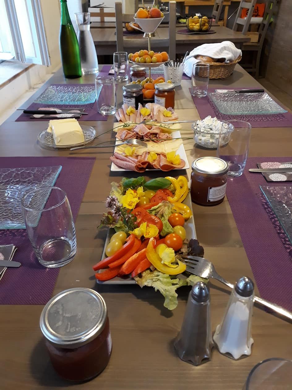 Megterített reggelizőasztal felvágottakkal, zöldségekkel, lekvárral és italokkal.