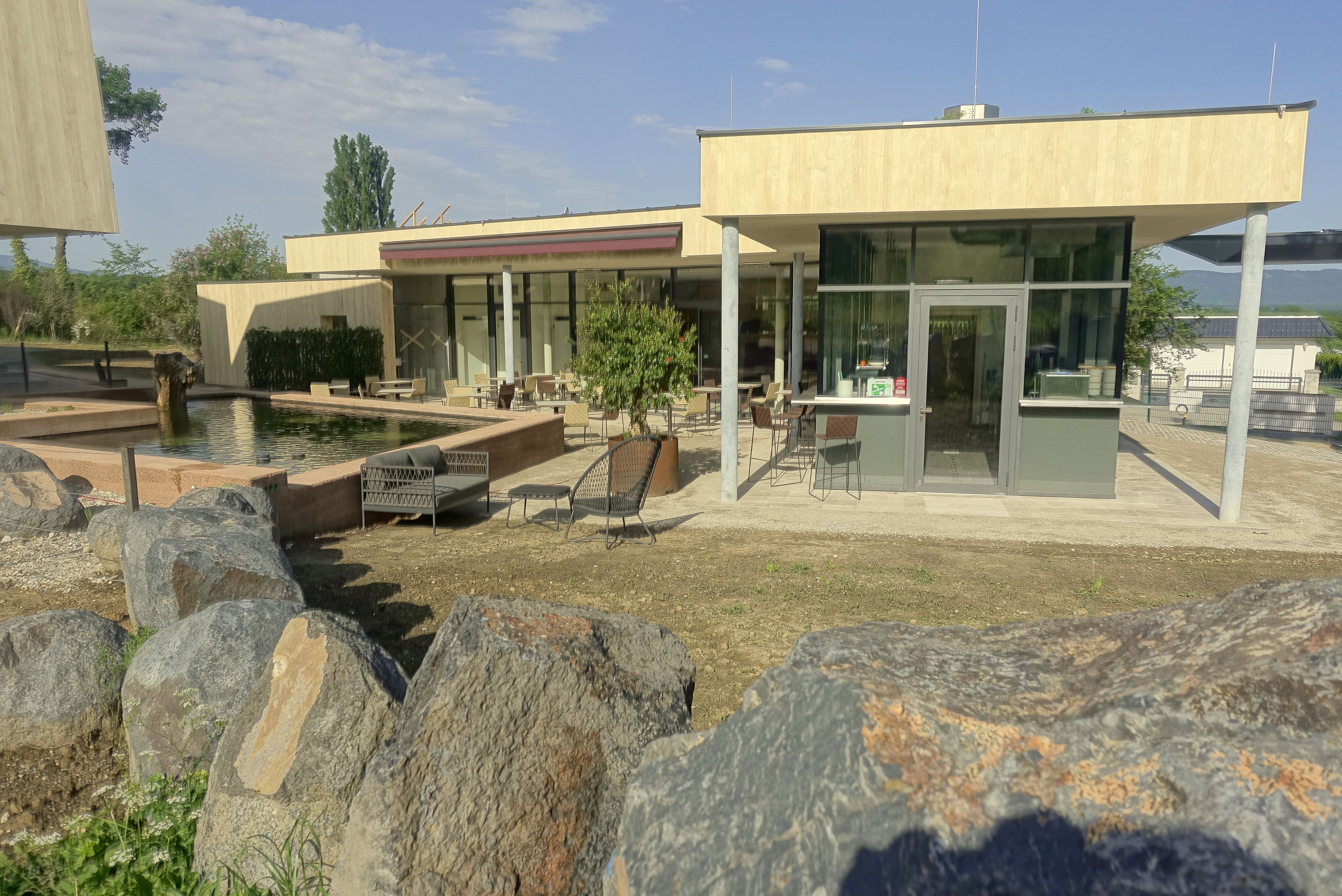 Modern veranda üvegfronttal és ülőfelülettel, sziklákkal és tóval körülvéve.