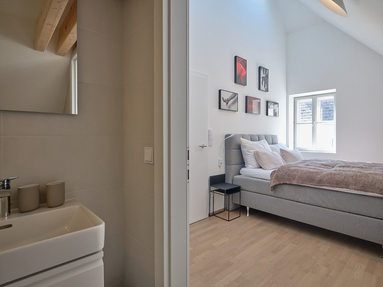 Modern hálószoba szürke ággyal és szomszédos fürdőszobával.