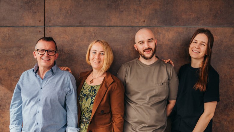 Négy ember áll mosolyogva egymás mellett egy barna fal előtt.