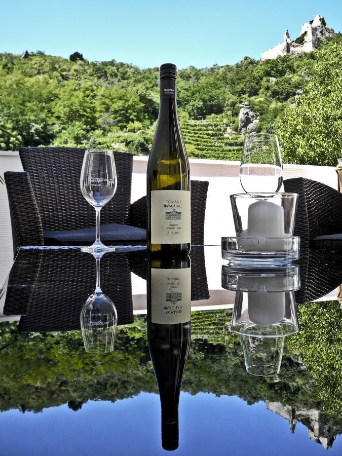 Borosüveg és poharak egy asztalon, kilátással a szőlőültetvényekre.