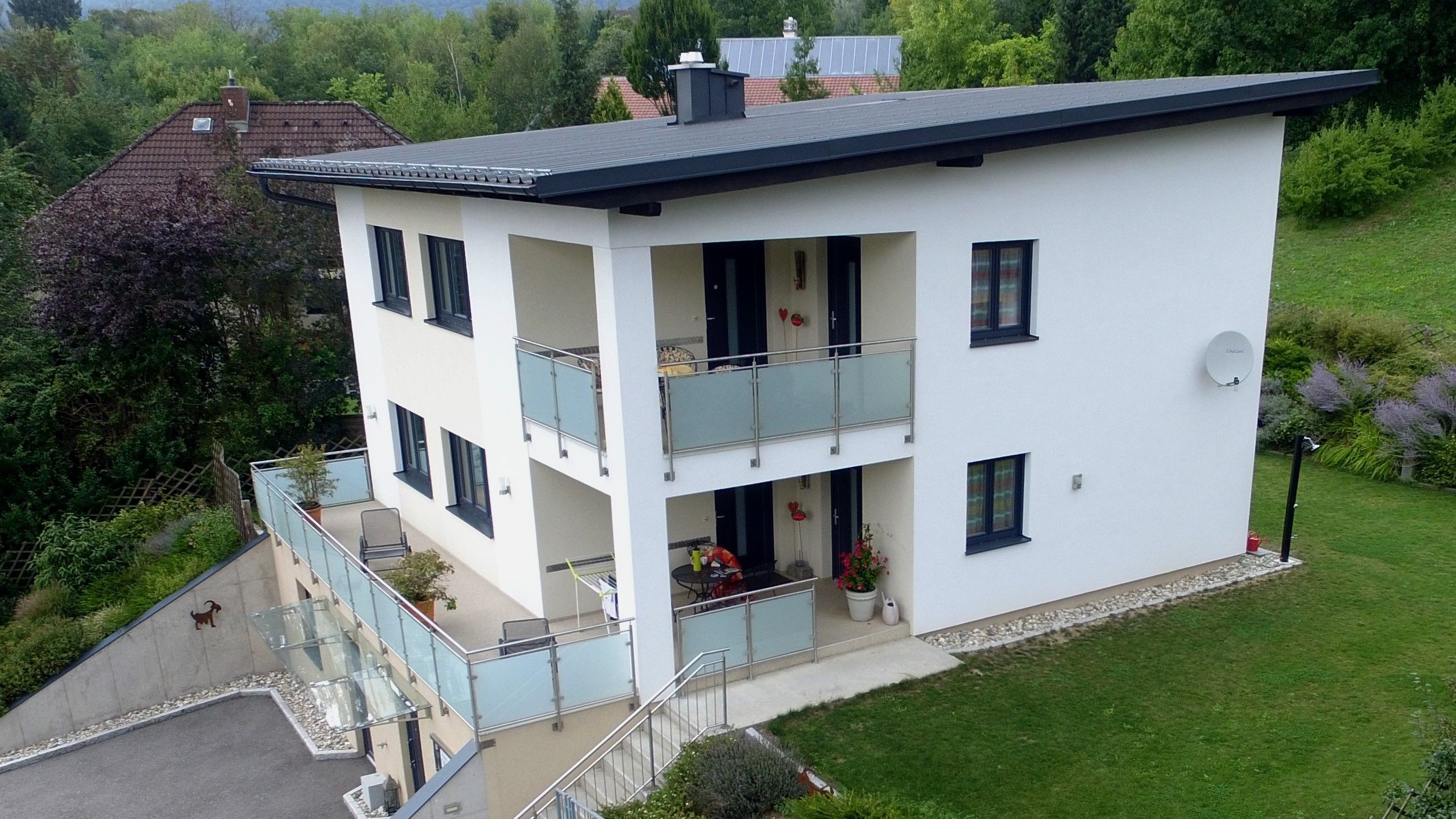 Drónfelvétel egy modern, kétszintes házról, erkéllyel és kerttel.