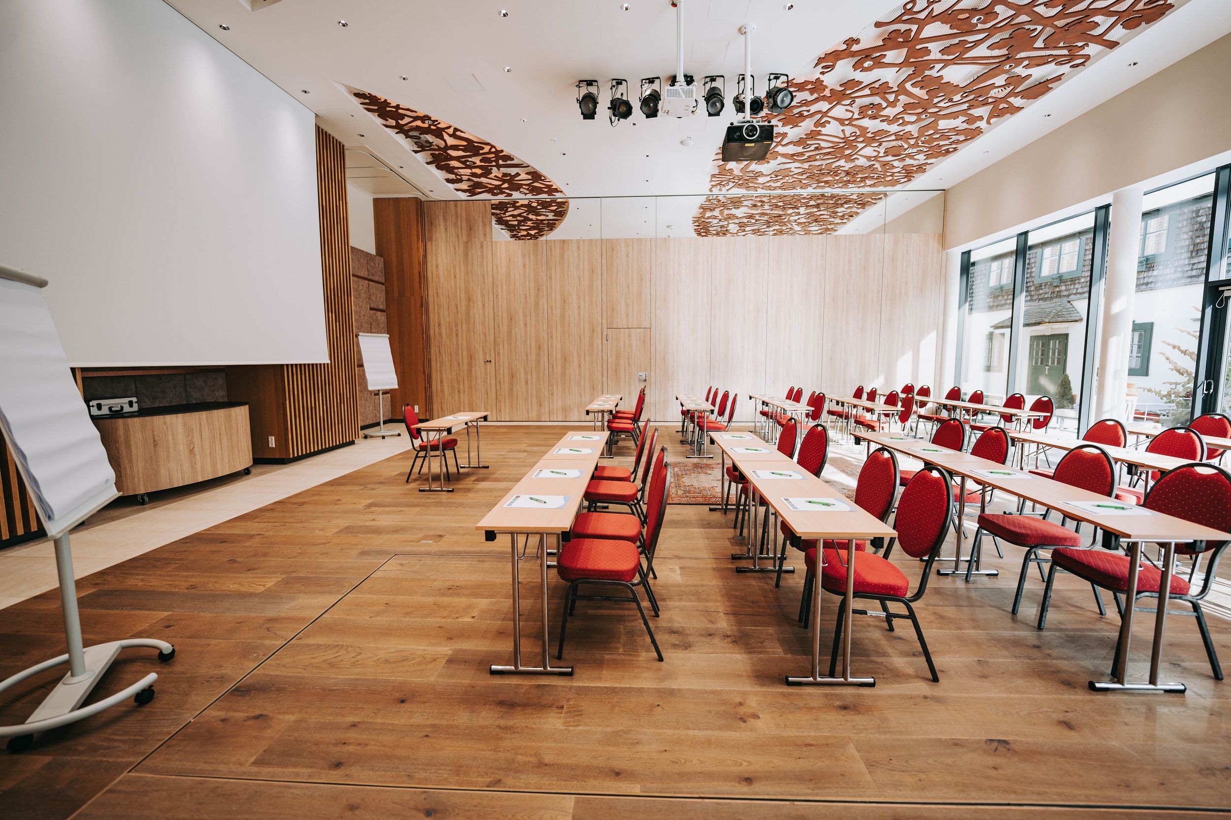Belső nézet egy modern konferenciateremről, piros székekkel és fapadlóval.