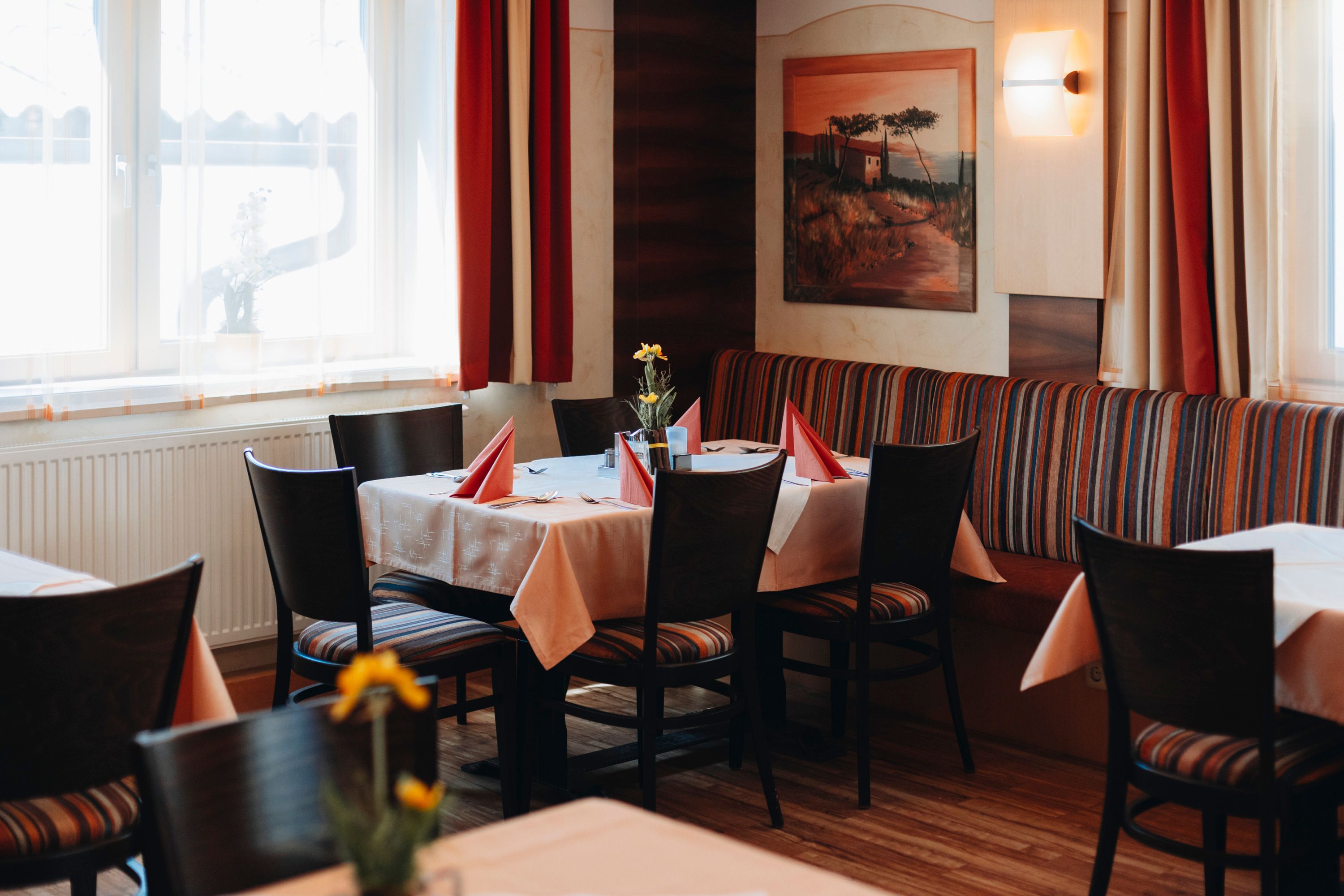 Hangulatos étterem terített asztallal, piros szalvétákkal és virágokkal.