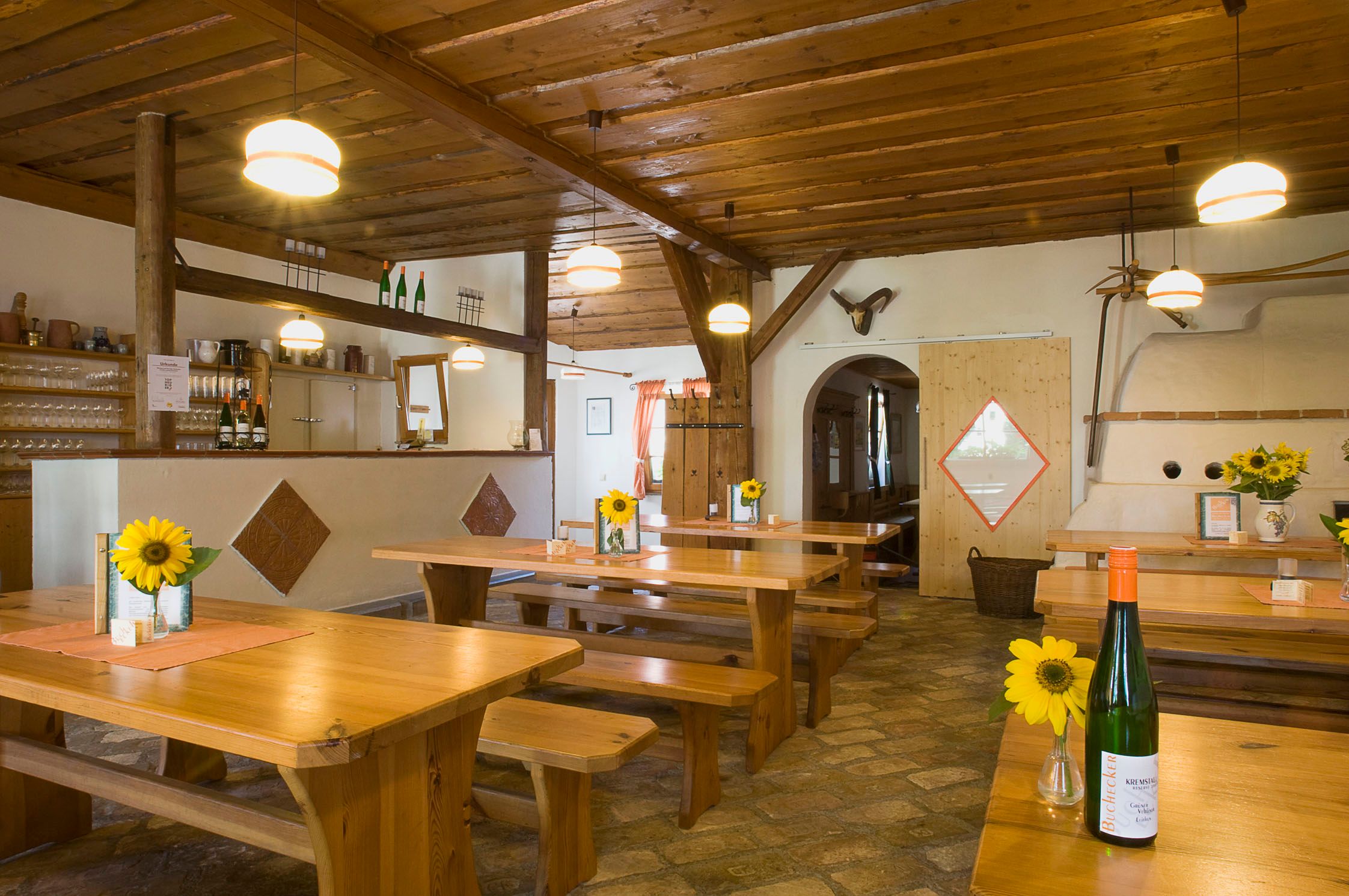 Egy hagyományos borozó belső nézete, faasztalokkal, napraforgókkal és borosüvegekkel.