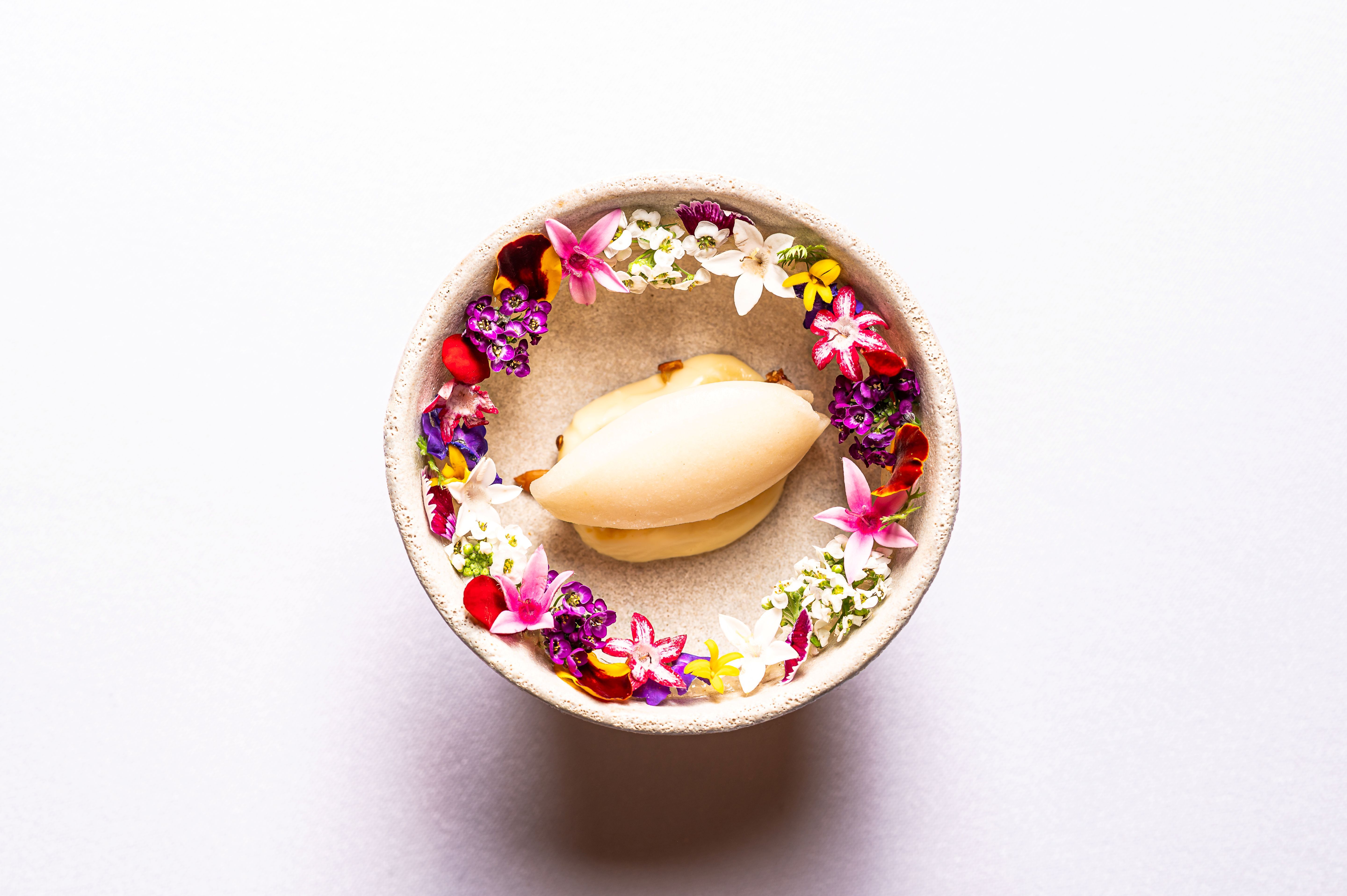 Színes ehető virágokkal körülvett desszert egy tálban.