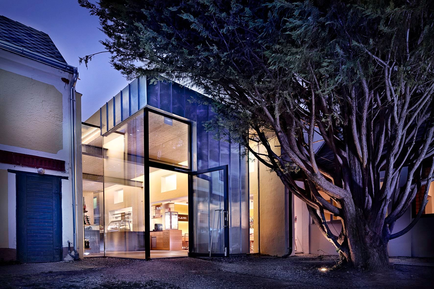 Egy épület modern üveghomlokzata éjszaka, fákkal körülvéve.
