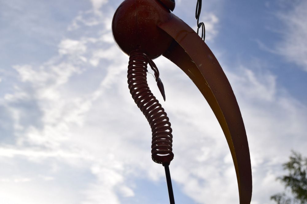 Közelkép egy spirál alakú elemmel rendelkező fémszoborról felhős égbolt előtt.