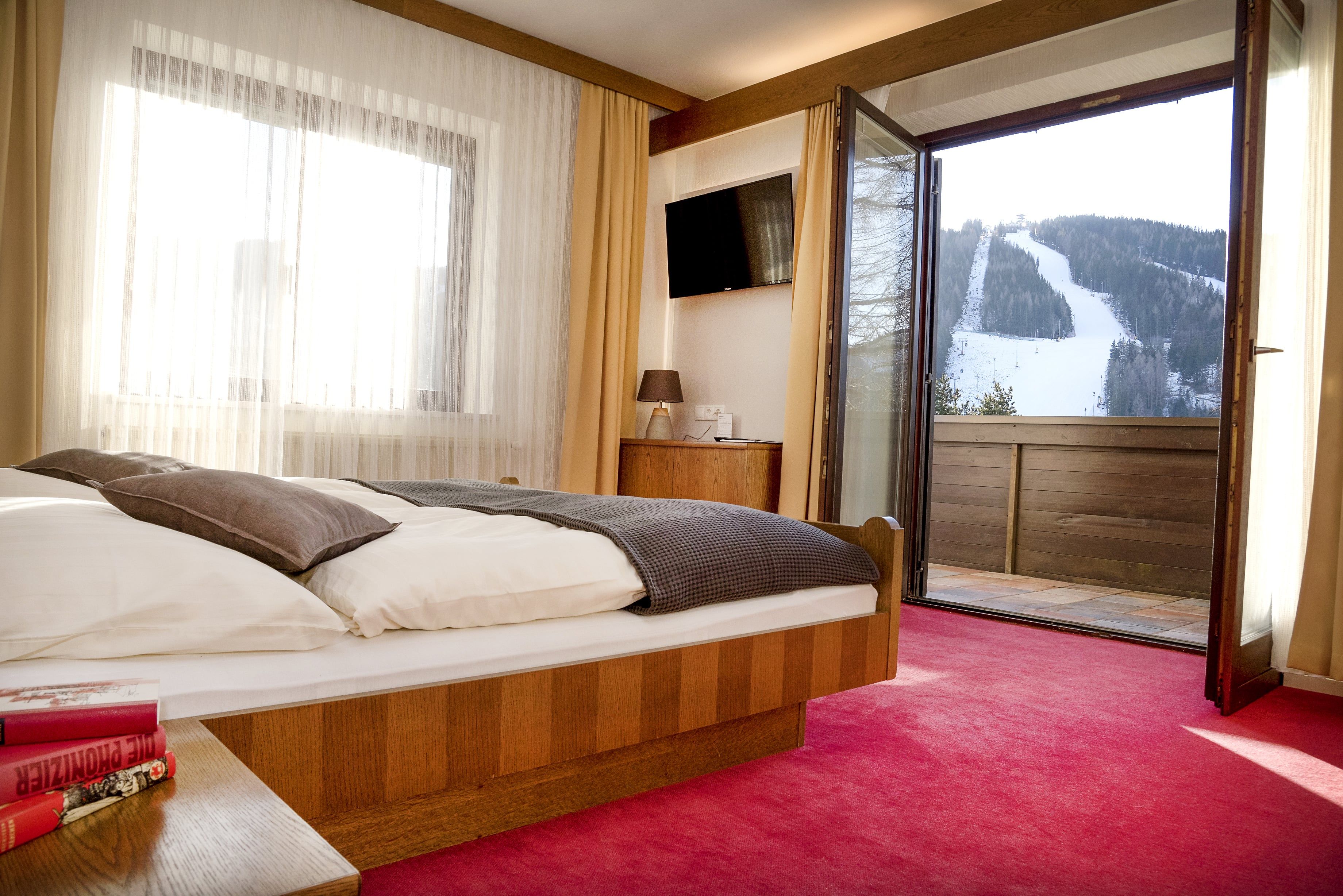 Hotelszoba nyitott erkéllyel és kilátással a hóval borított sípályára.