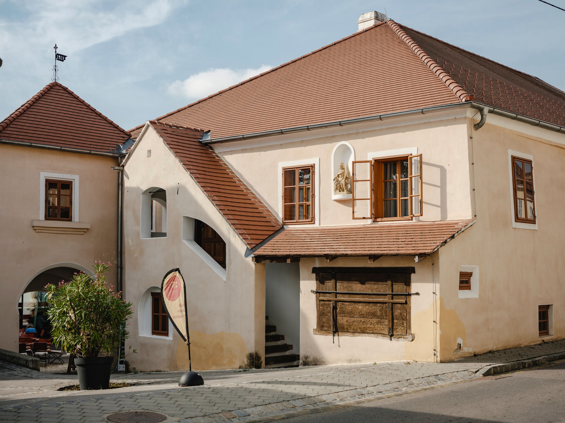 Történelmi épület vörös cseréptetőkkel és nyitott ablakokkal.
