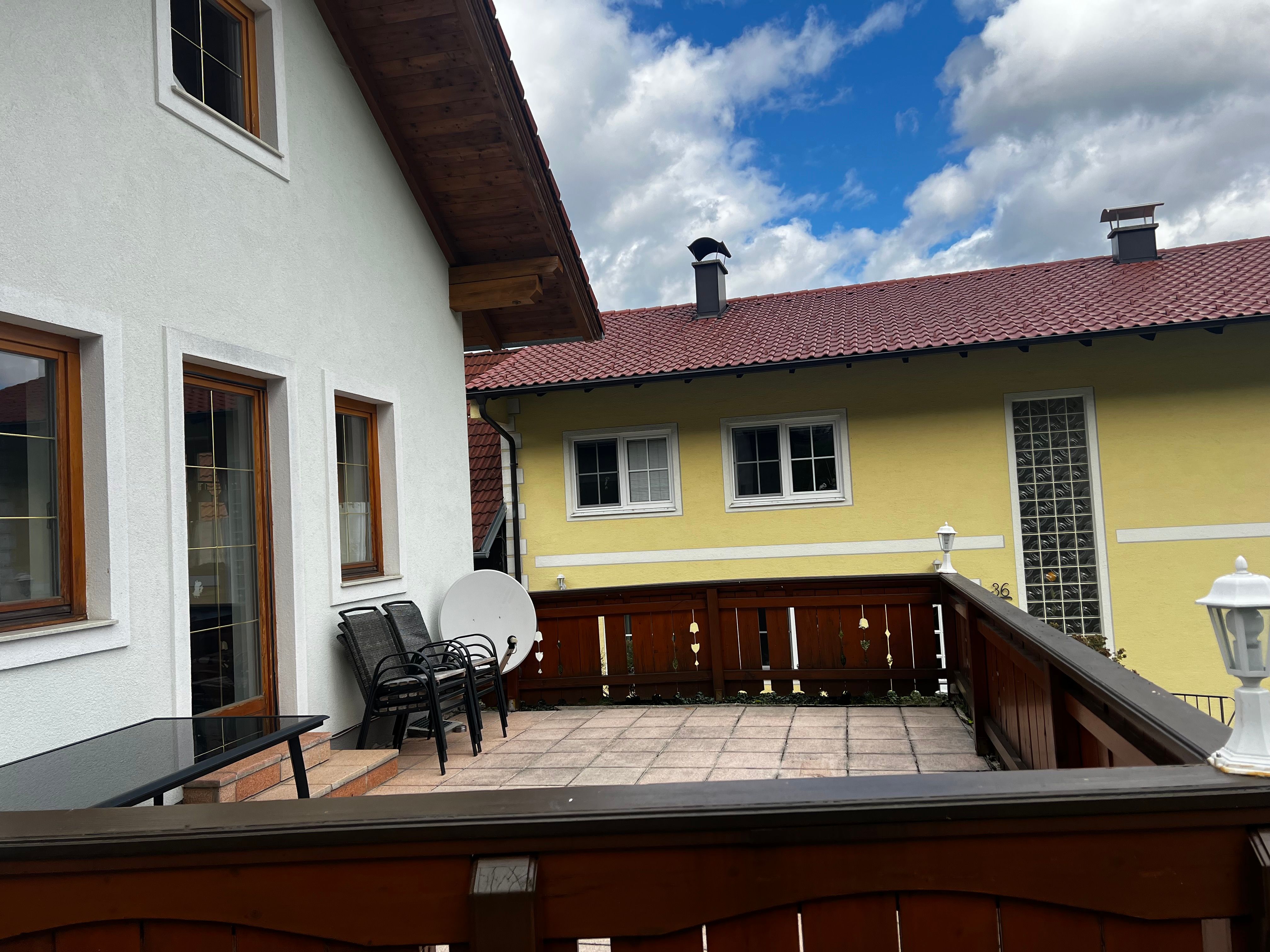 Egy lakás terasza fából készült bútorokkal és kilátással egy sárga, piros tetejű szomszédos házra.