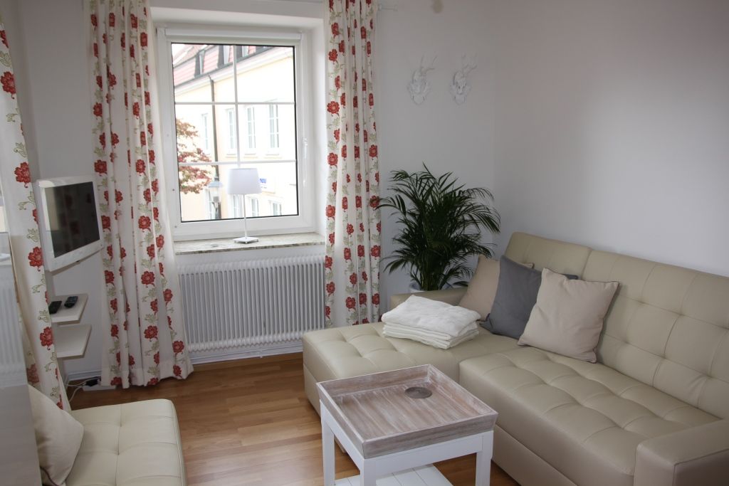 Világos nappali bézs színű kanapéval, párnákkal, dohányzóasztallal és függönyös ablakkal.