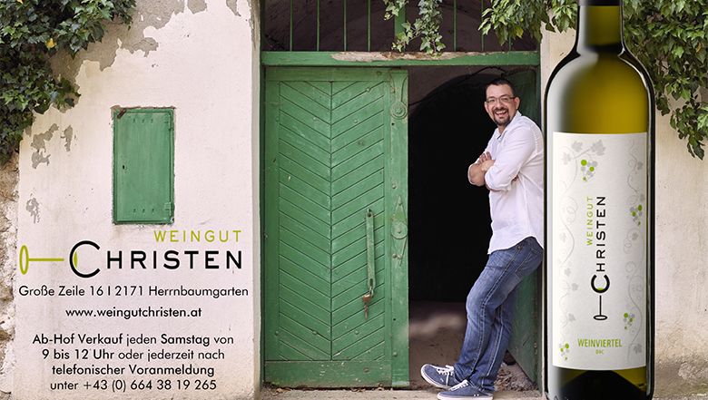 Egy férfi egy zöld ajtónak támaszkodik egy "Weingut Christen" feliratú borosüveg mellett.